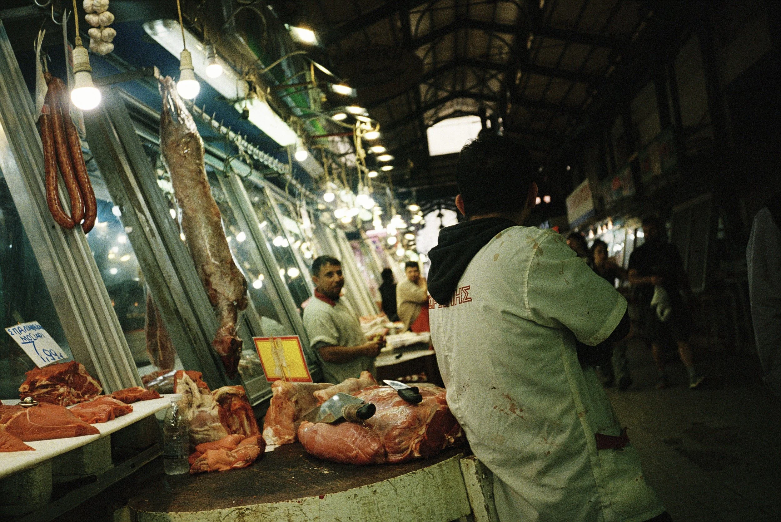 Blick auf einen Fischmarkt mit Fleisch und Fisch. Mehrere Verkäufer und Kunden sind im Hintergrund zu sehen, das Marktstand ist mit Fleischwaren gefüllt.