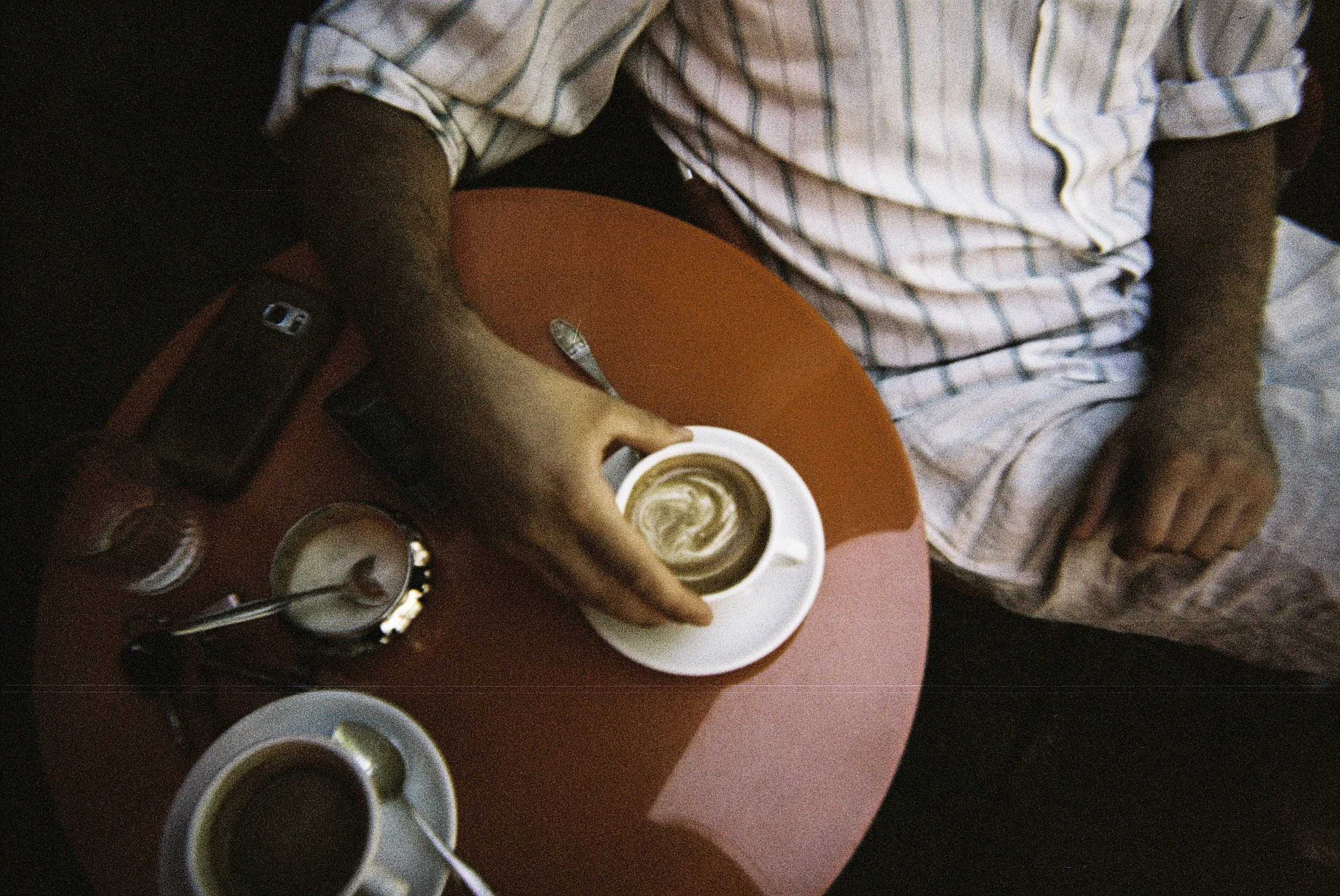 Person, die Kaffee in eine Tasse gießt, auf einem rot-schwarzen Tisch mit mehreren Kaffeetassen.