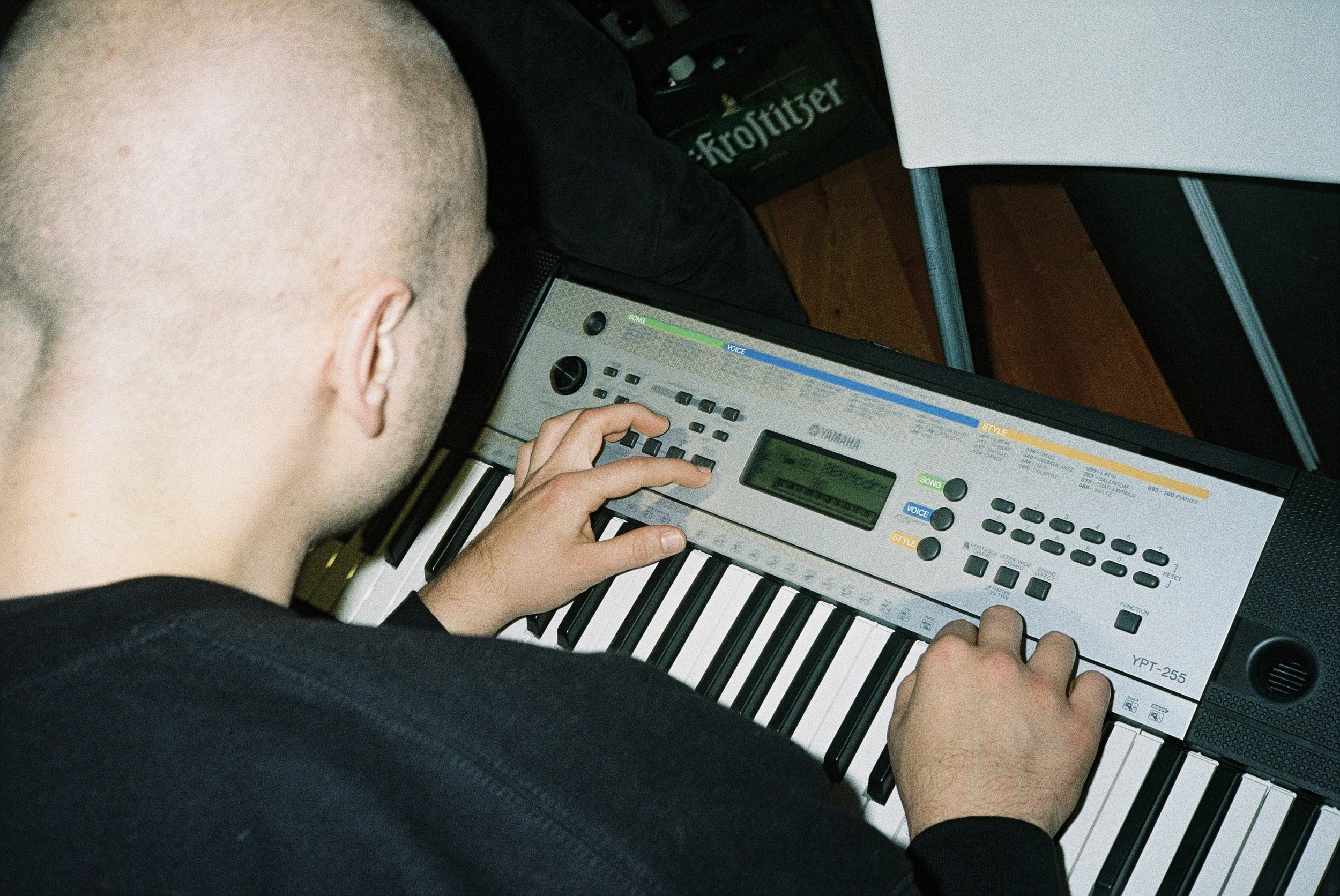 Eine Person spielt auf einem Yamaha Keyboard. Im Hintergrund ist eine Packung mit einer Flasche Froschlikör sichtbar.