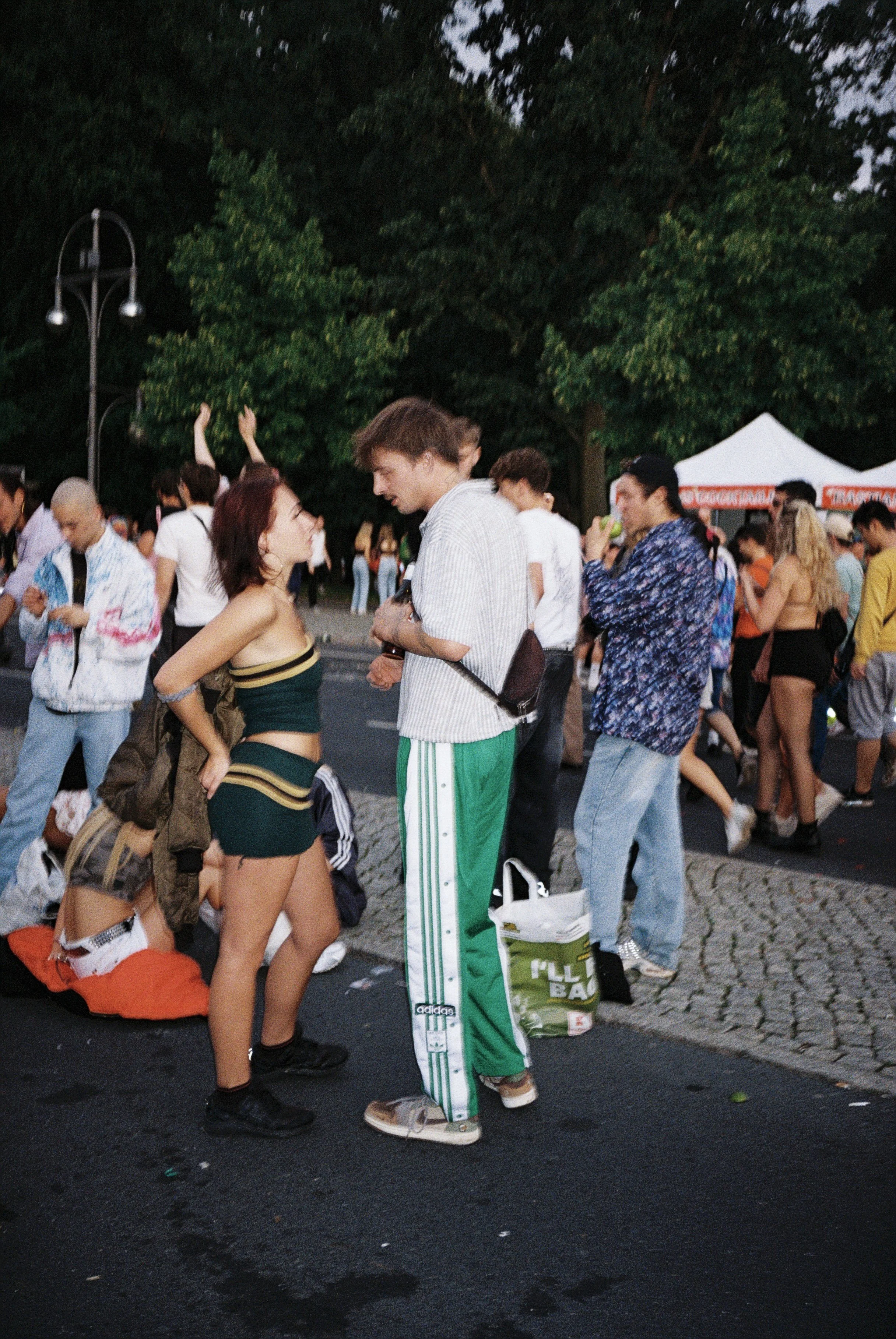 Menschen bei einem Open-Air-Festival im Park, einige unterhalten sich, andere entspannen, im Hintergrund sind Tische und ein Zelt zu sehen.