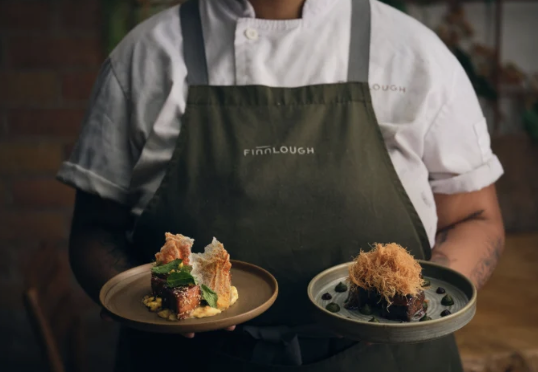 Chef holding two plates with gourmet dishes in a restaurant setting.