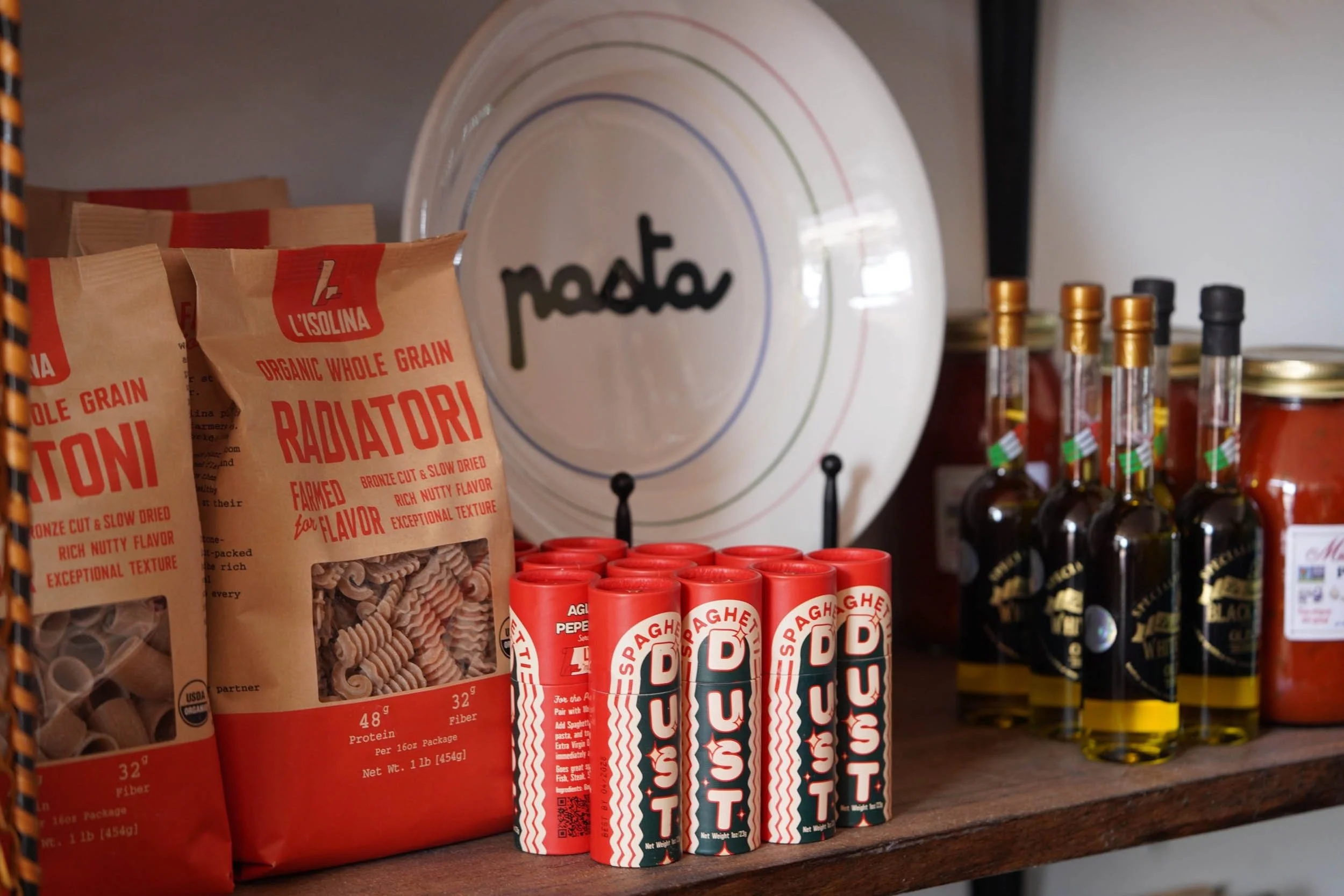 Shelf displaying various food products including L'Isolina organic whole grain pasta, Spaghett D tubes, and bottled sauces or oils.