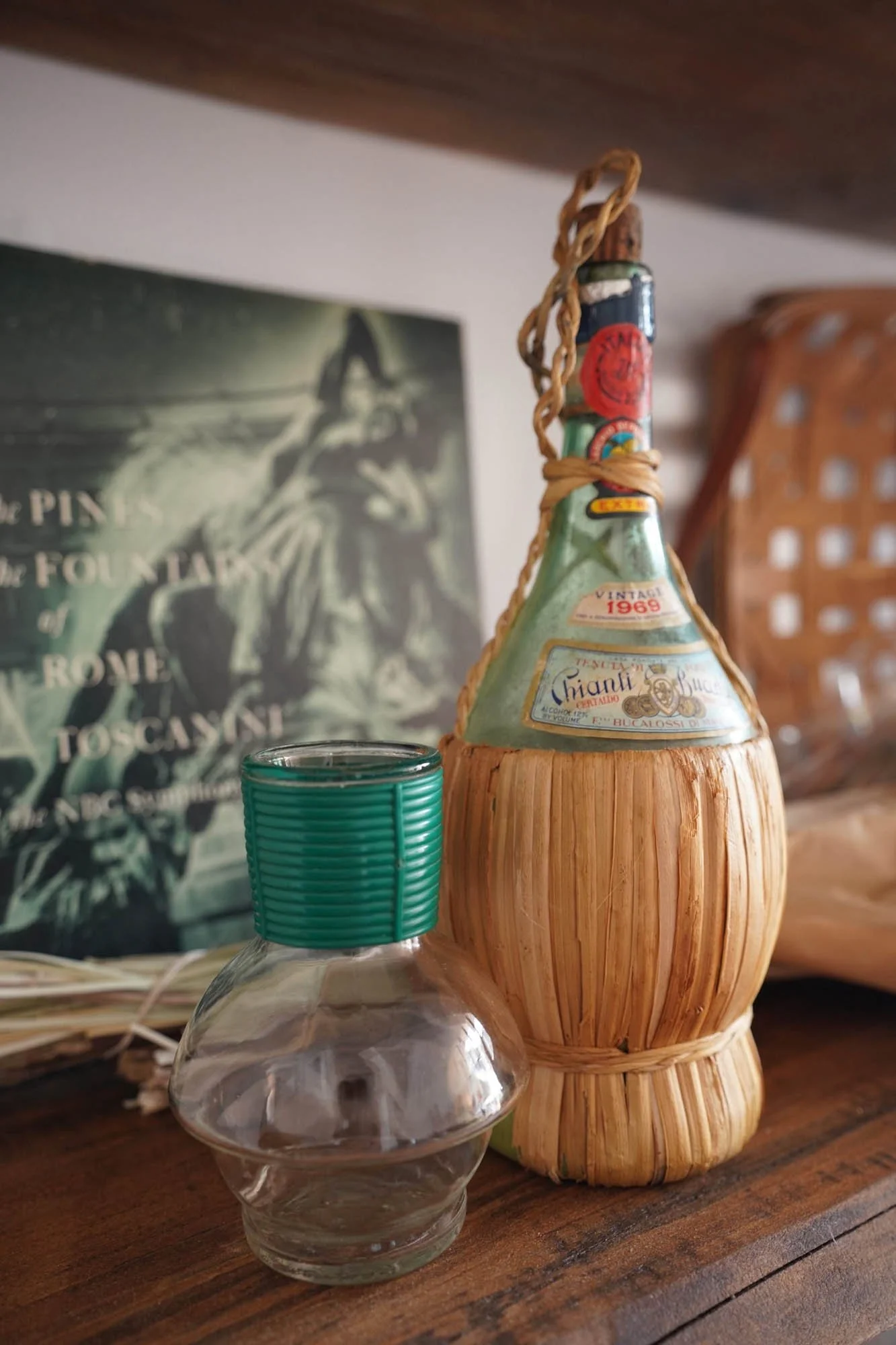 A glass bottle with a green cap, a bamboo and wood container with a label, and a piece of art in the background with text.