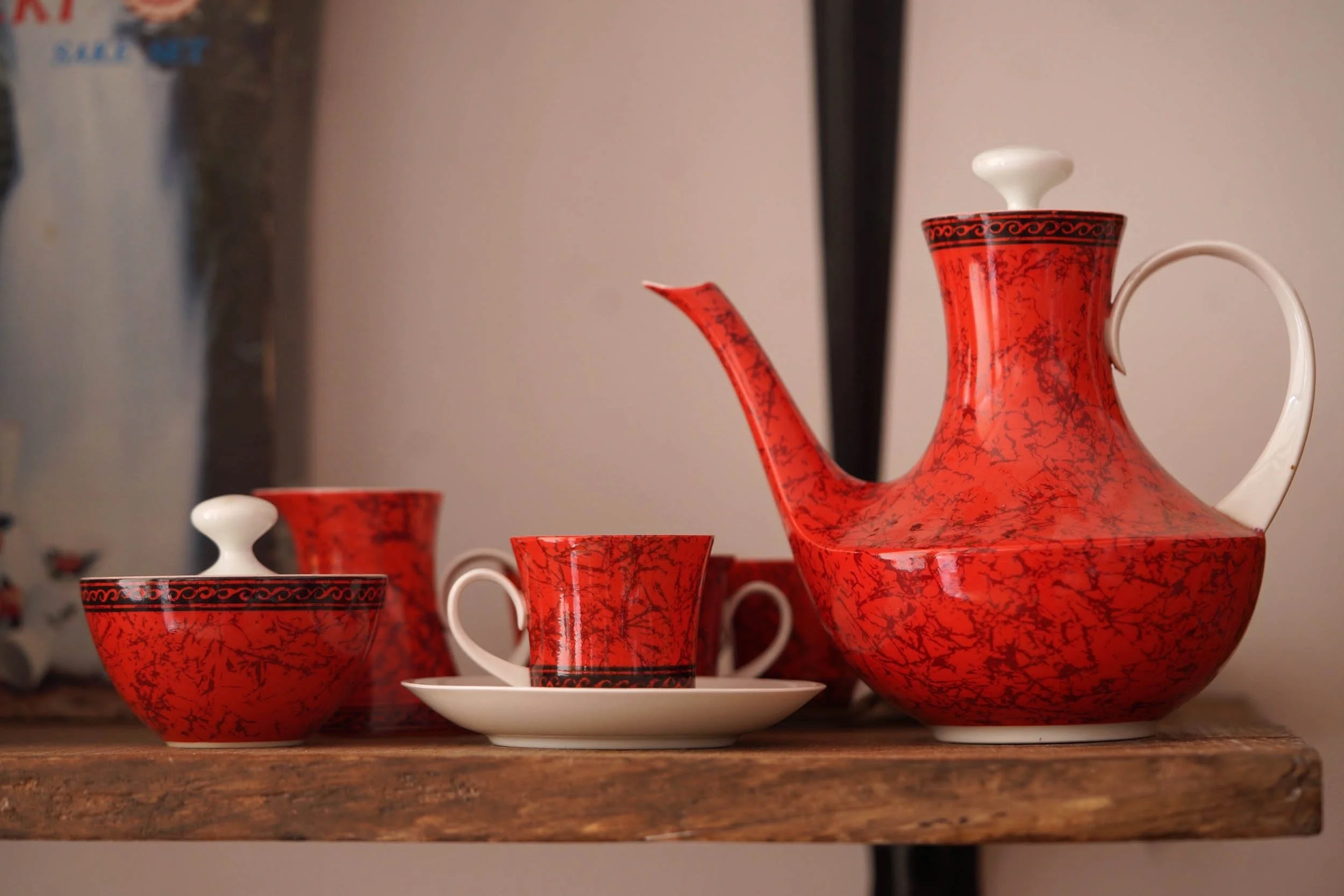 Red and black patterned tea set including a teapot, cups, saucer, and sugar bowl displayed on a wooden surface.