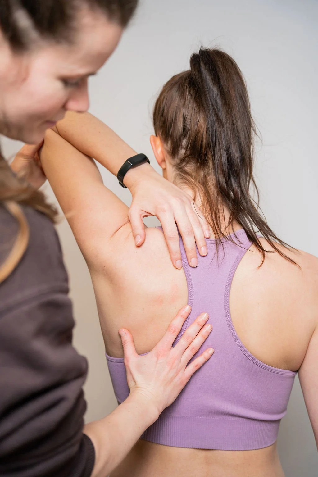 Een medische professional onderzoekt de rug van een vrouw die een paarse sporttop draagt.