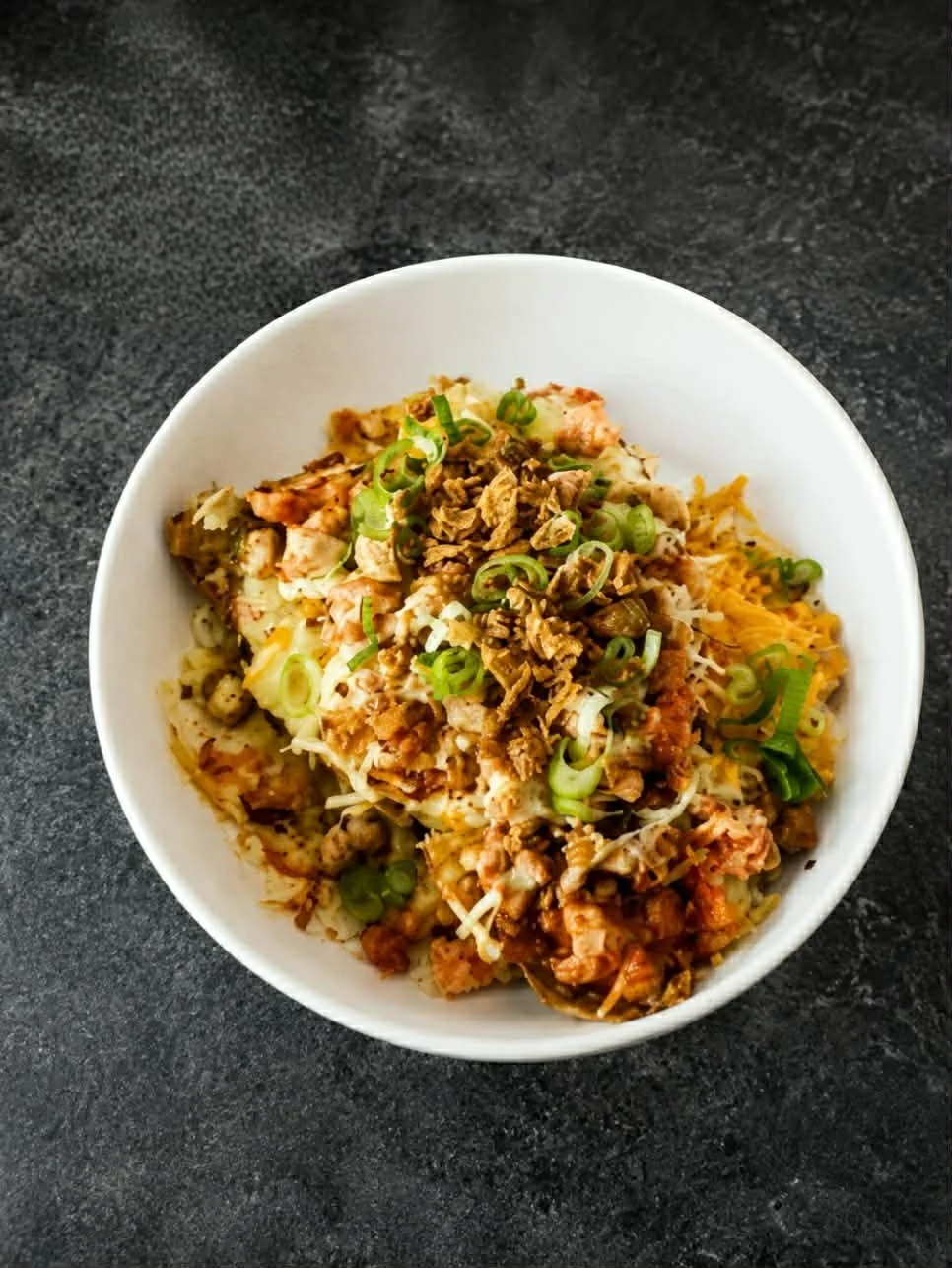 Bord met een gerecht met rijst, vlees, gesneden groene uien, kaas en saus