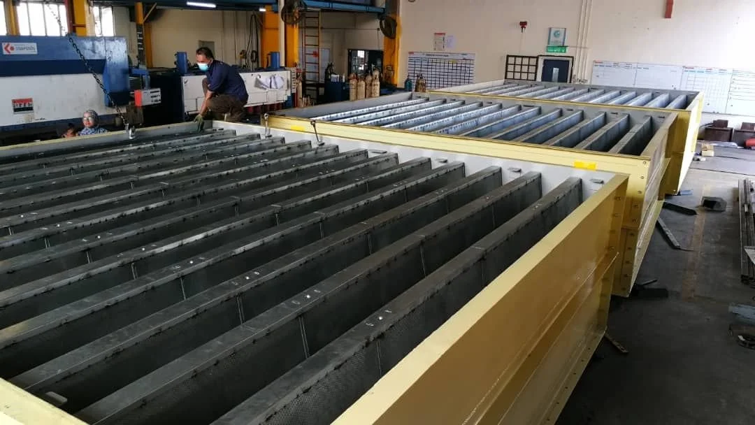 Industrial manufacturing facility with large metal roller conveyor system and workers handling equipment in the background.