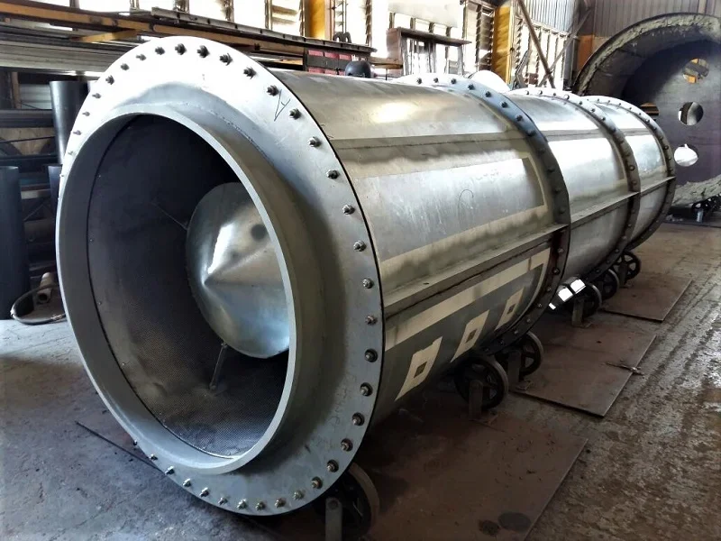 Large metallic rocket engine with a cylindrical shape, mounted on a wheeled cart inside a workshop with tools and machinery in the background.