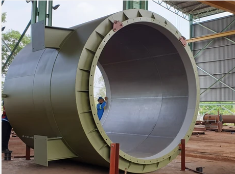 Large industrial cylindrical tank with open end, inside a warehouse under construction.