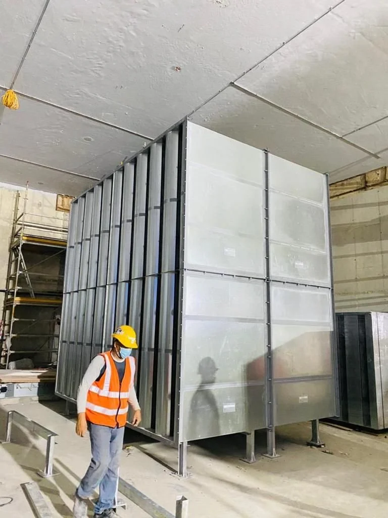 Construction worker wearing safety helmet and vest standing inside a building with large metal structure panels.