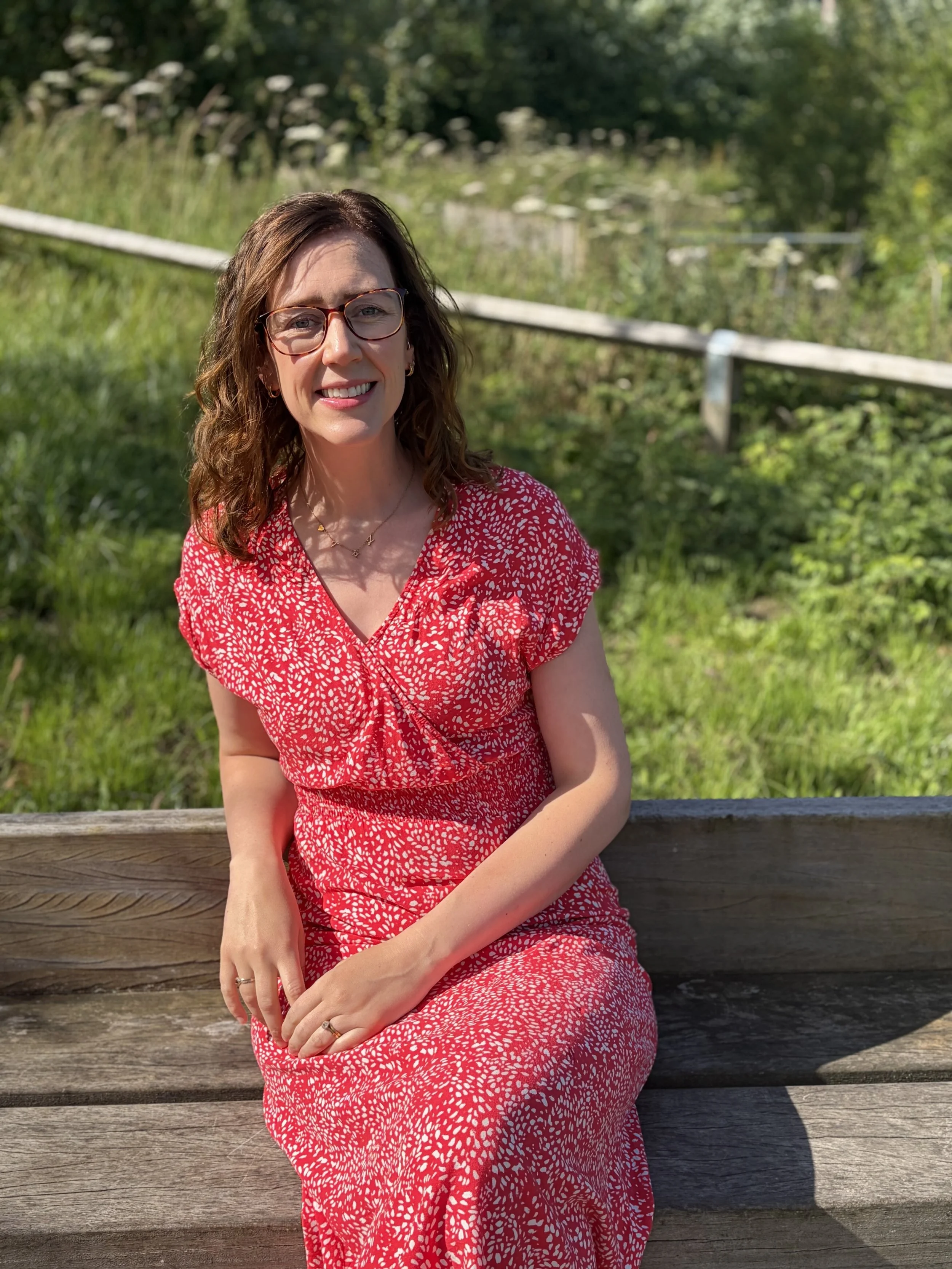 Clinical Hypnotherapist sat on bench in a meadow smiling at camera