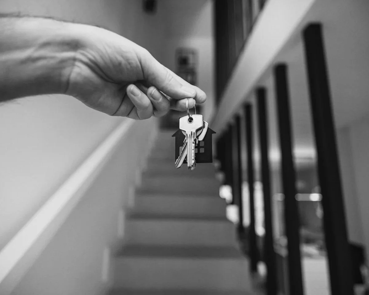 A hand holding a set of keys with keychains in front of a staircase with black balusters.