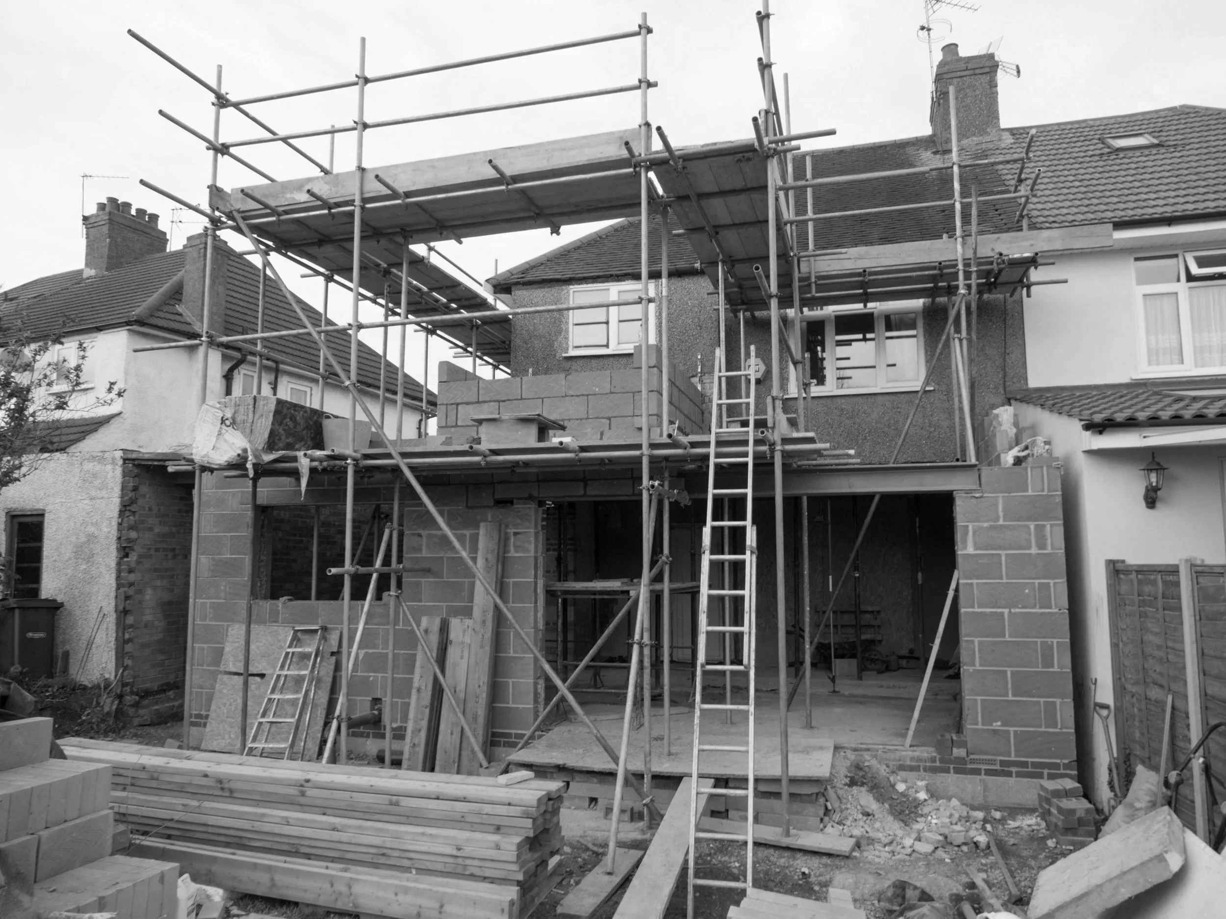 Residential house under construction with scaffolding and building materials in the yard.