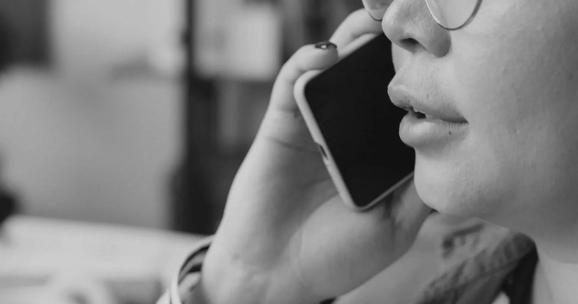 Close-up black and white photo of a person's face with glasses, holding a smartphone to their ear.
