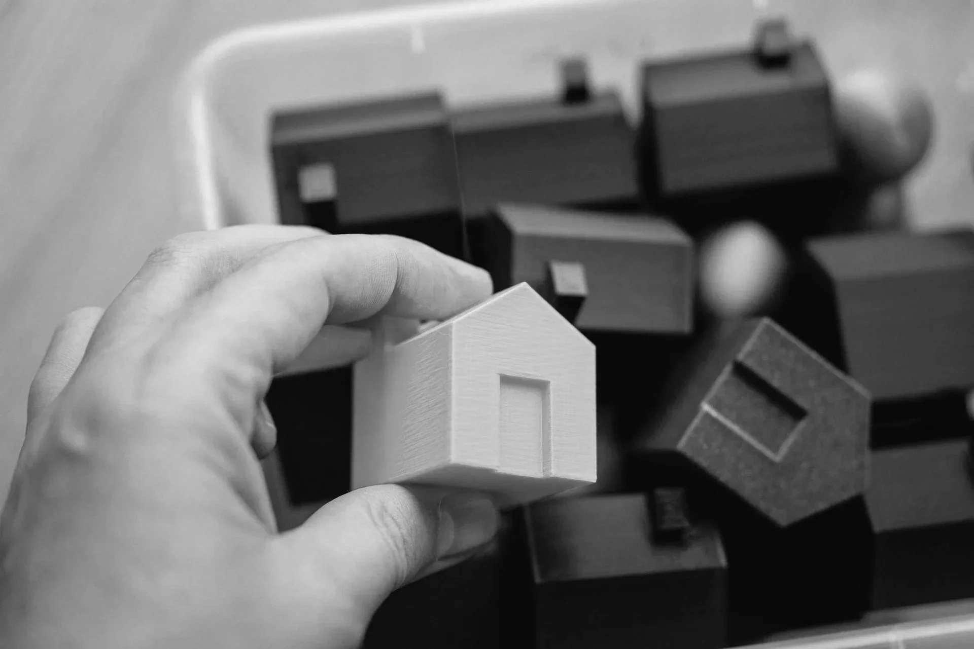 Close-up of a person's hand holding a small white house-shaped object among other similar objects on a table.
