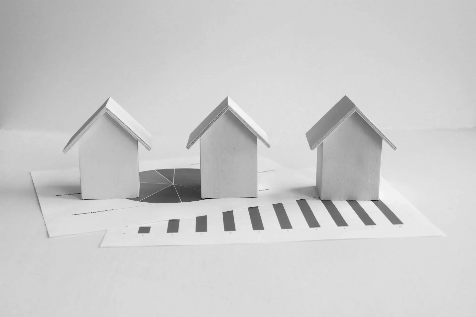 Three small, white, paper model houses placed on a printed sheet of paper with charts and graphs.