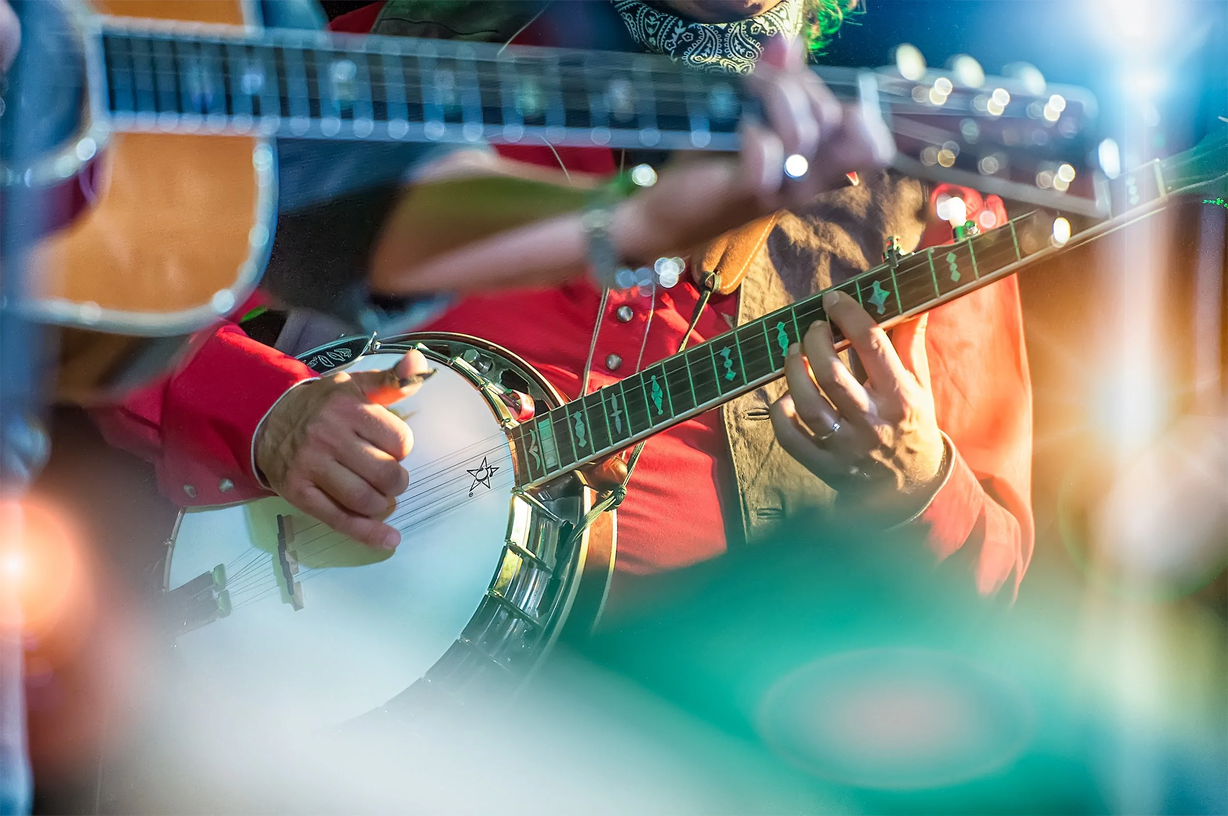 Person wearing a red jacket playing an acoustic guitar with a green fretboard.