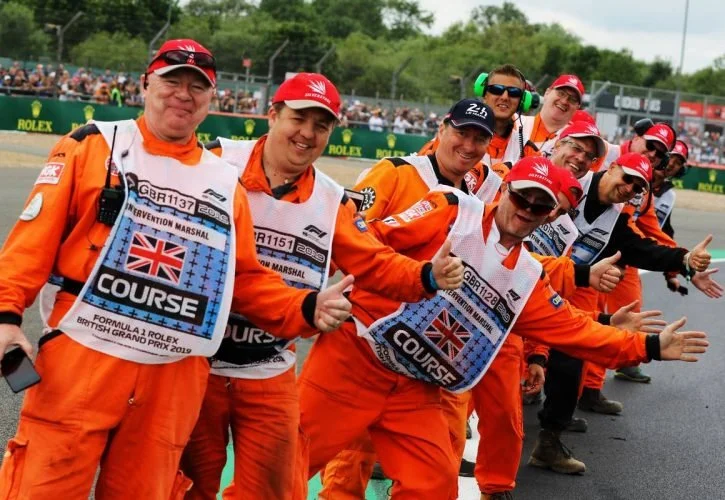 Race marshals in orange uniforms gathered trackside during a motorsports event.