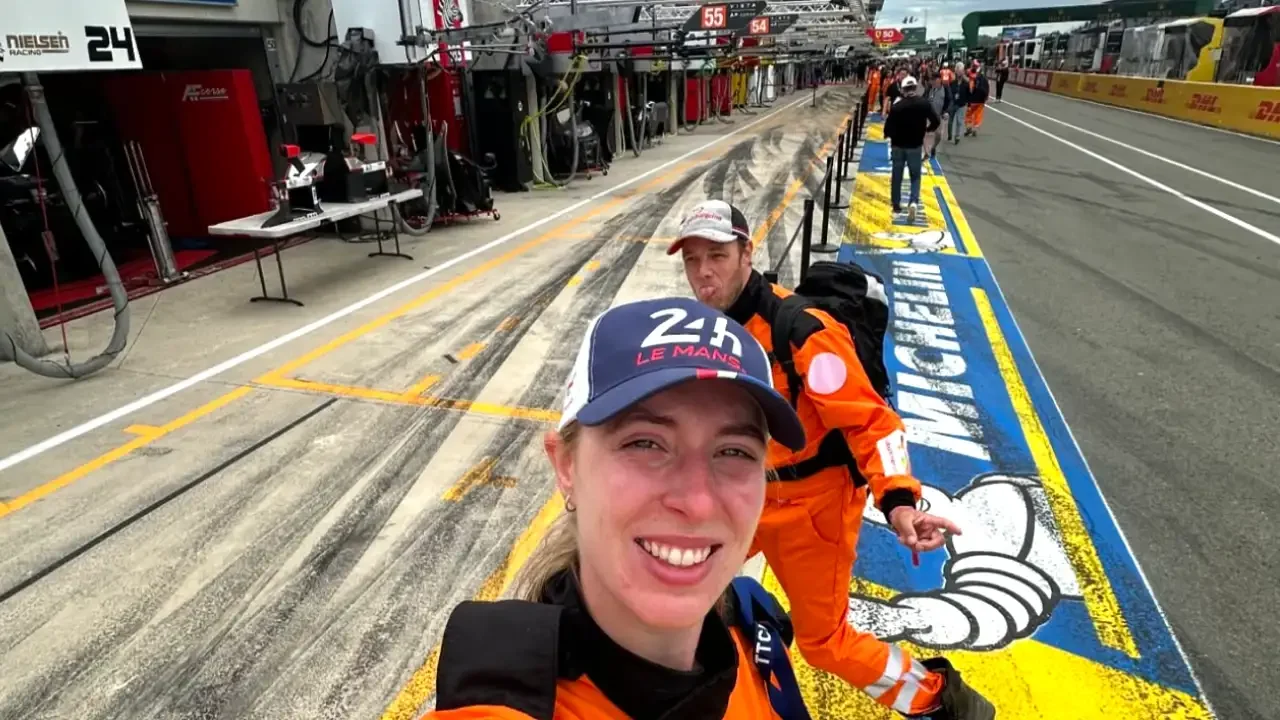 Two race-event team members taking a selfie in pit lane during a motorsports event.