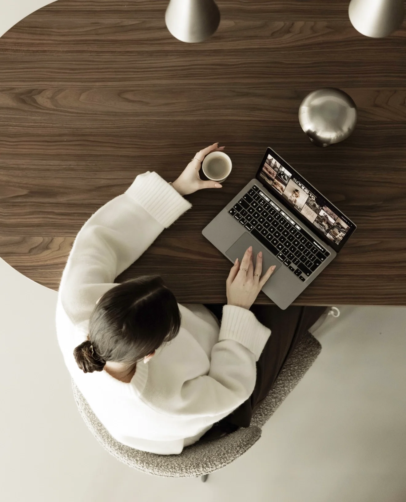 Britt Breemen social media manager, zit aan een houten tafel met een open laptop en een beker, haar hand op de trackpad, terwijl een kind naast haar zit en naar het scherm kijkt.
