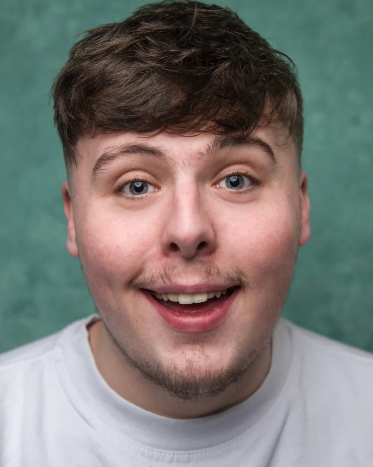 Headshot of actor Cieran Low smiling in a white top against a muted green background.