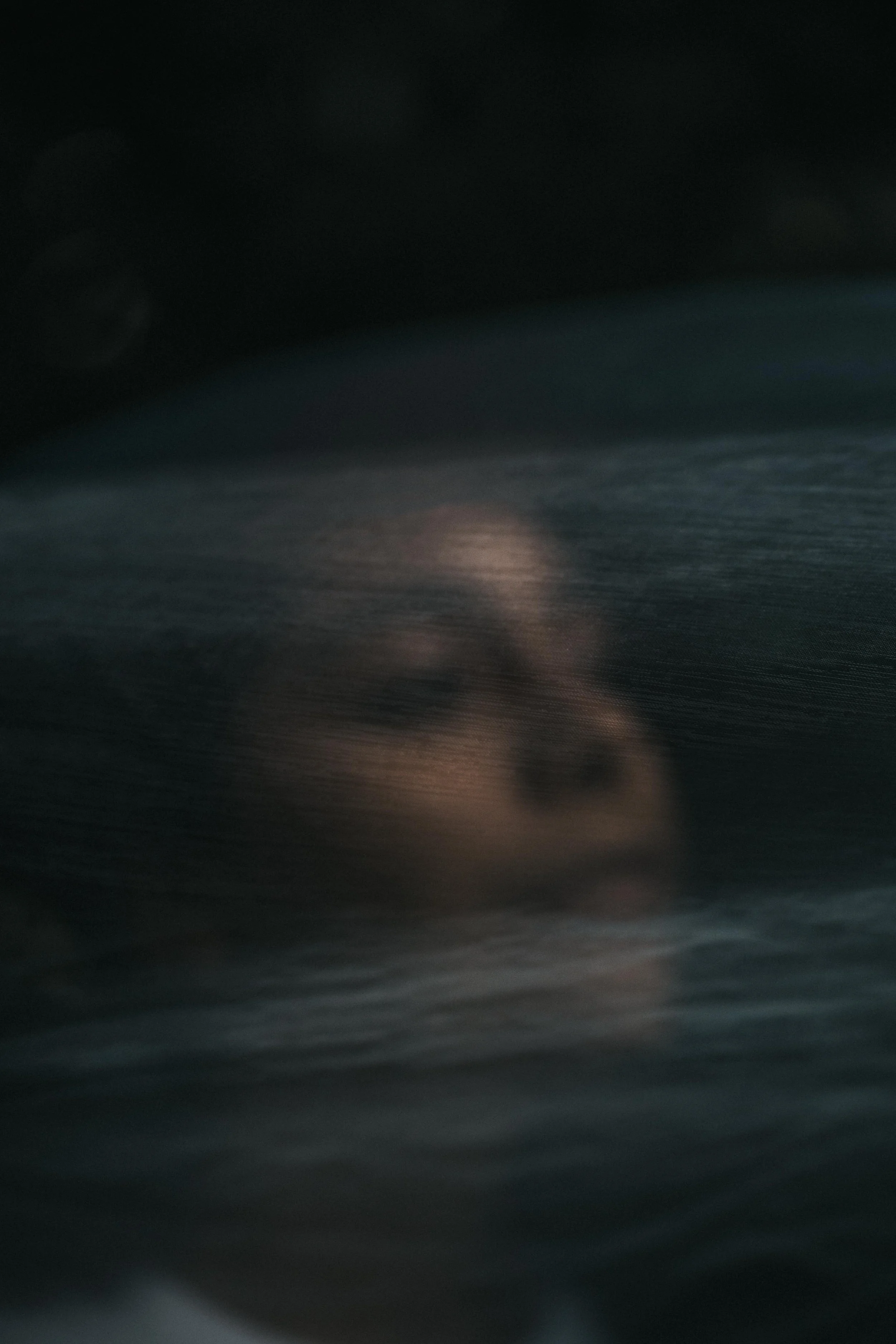 A dark, blurry photo of a body of water with faint lights or reflections on its surface.