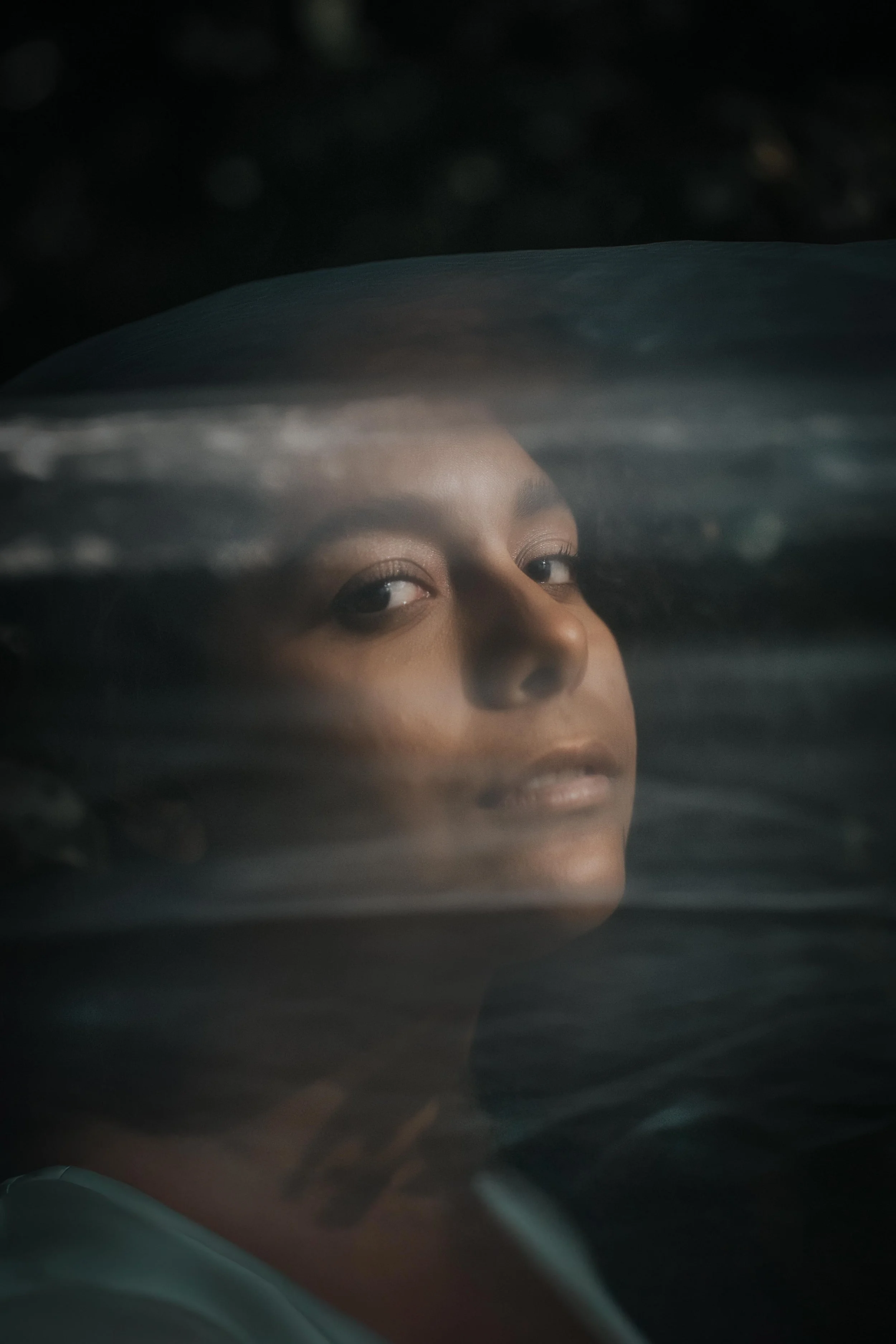 Partial view of a person's face, mainly showing the eyes and nose, through a blurred, dark surface or window.