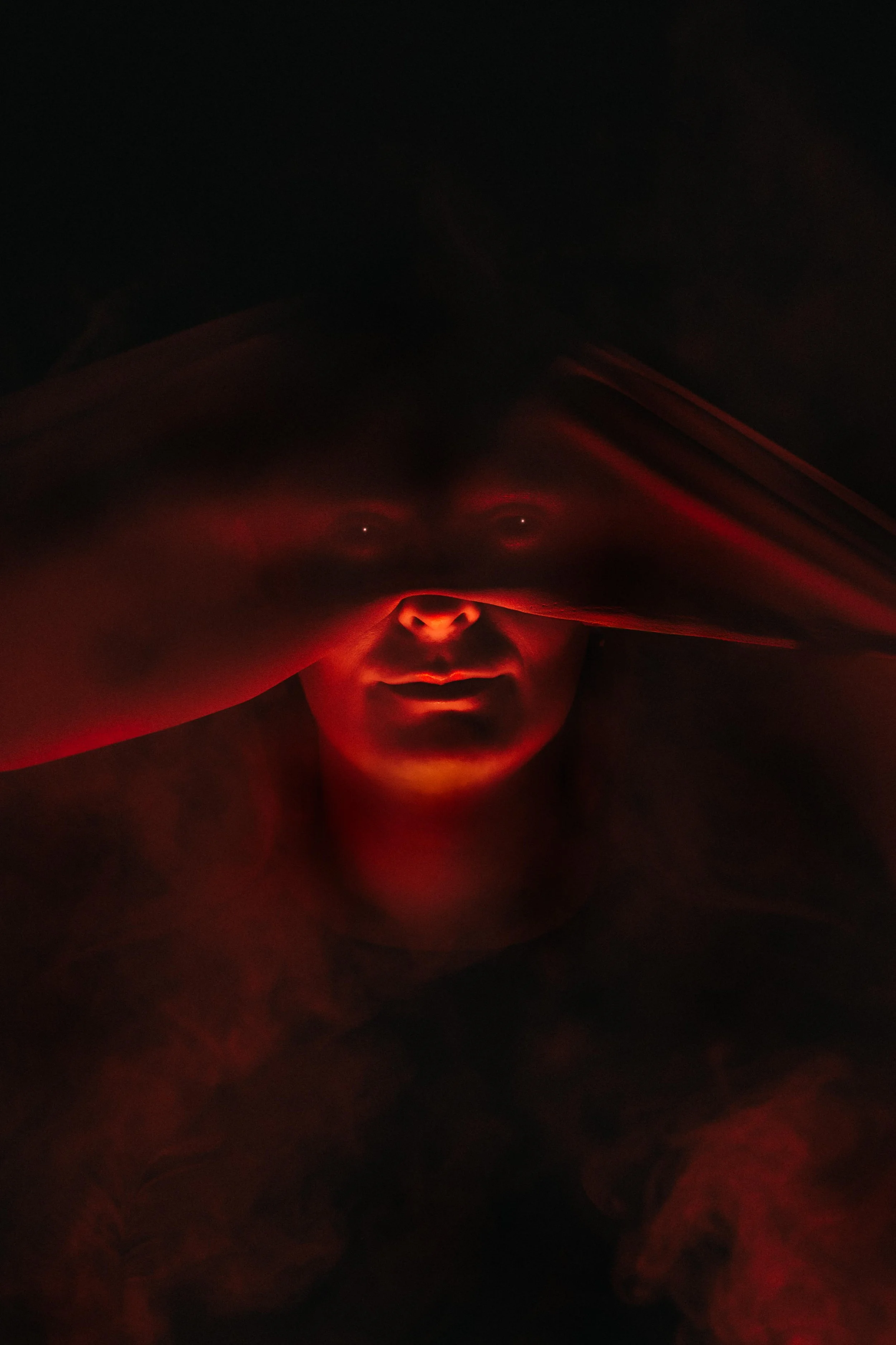 A person's face illuminated by red light in a dark environment, with some facial features visible.