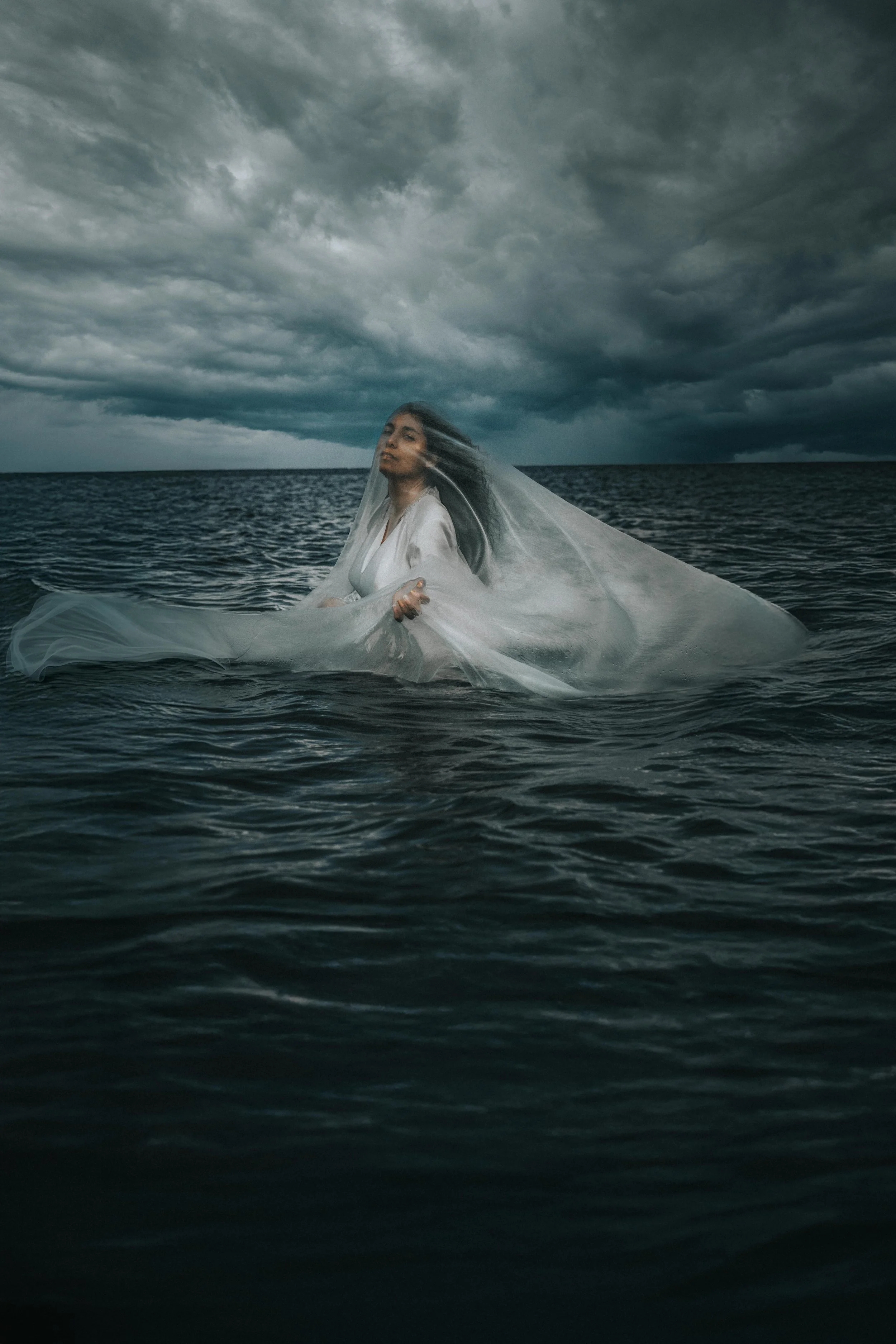 Woman in a white dress standing in the water under a dark, stormy sky.