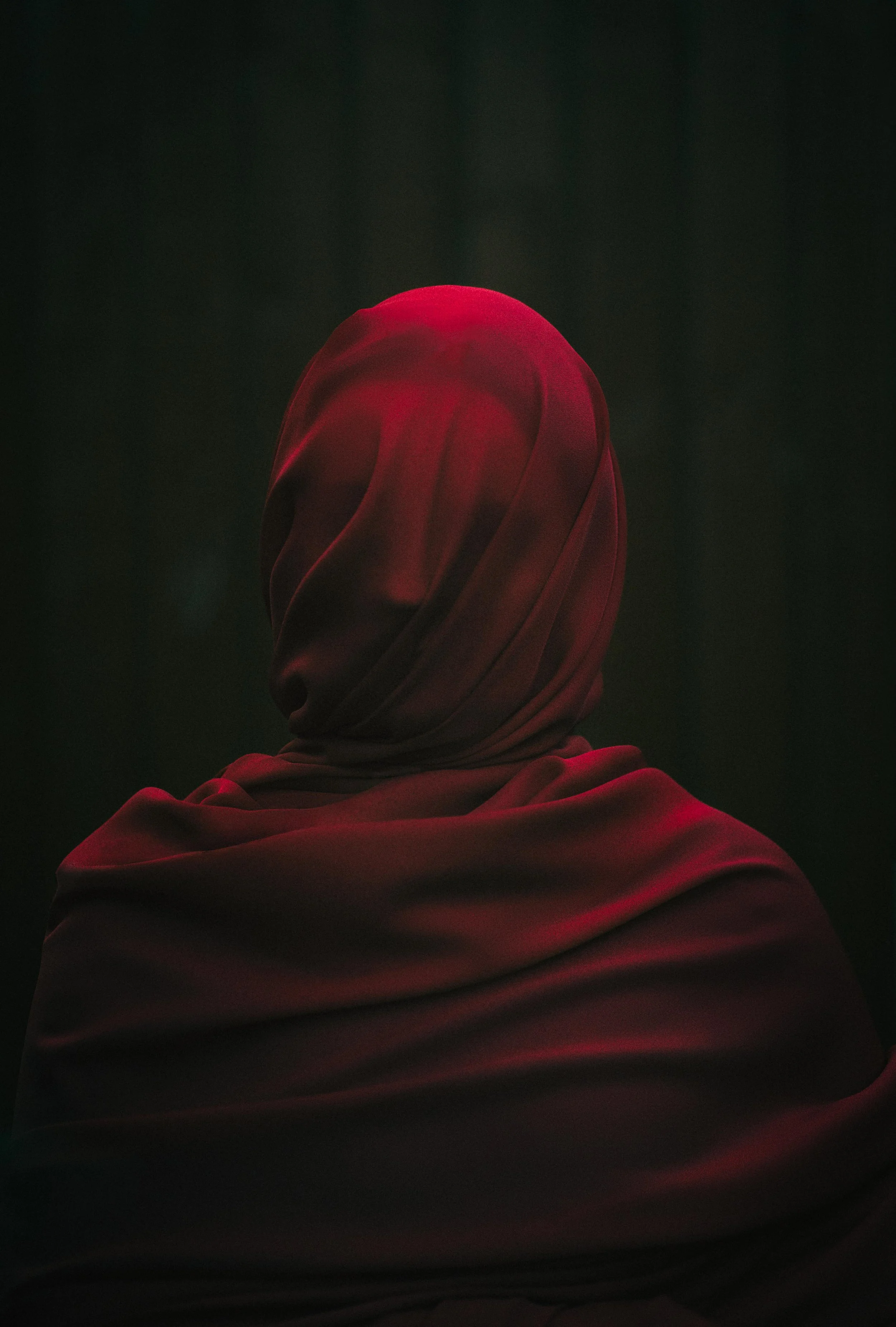 A person in a red headscarf and matching clothing against a dark background.