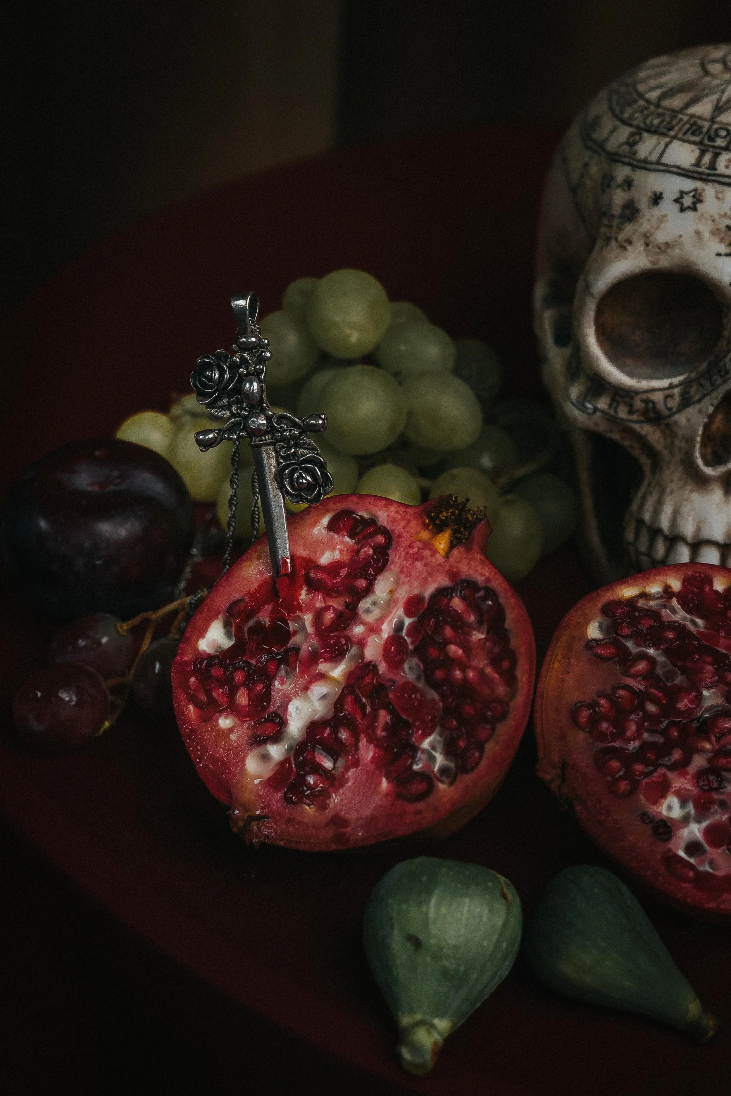 Close-up of pomegranates, grapes, and a skull decoration on a dark surface.