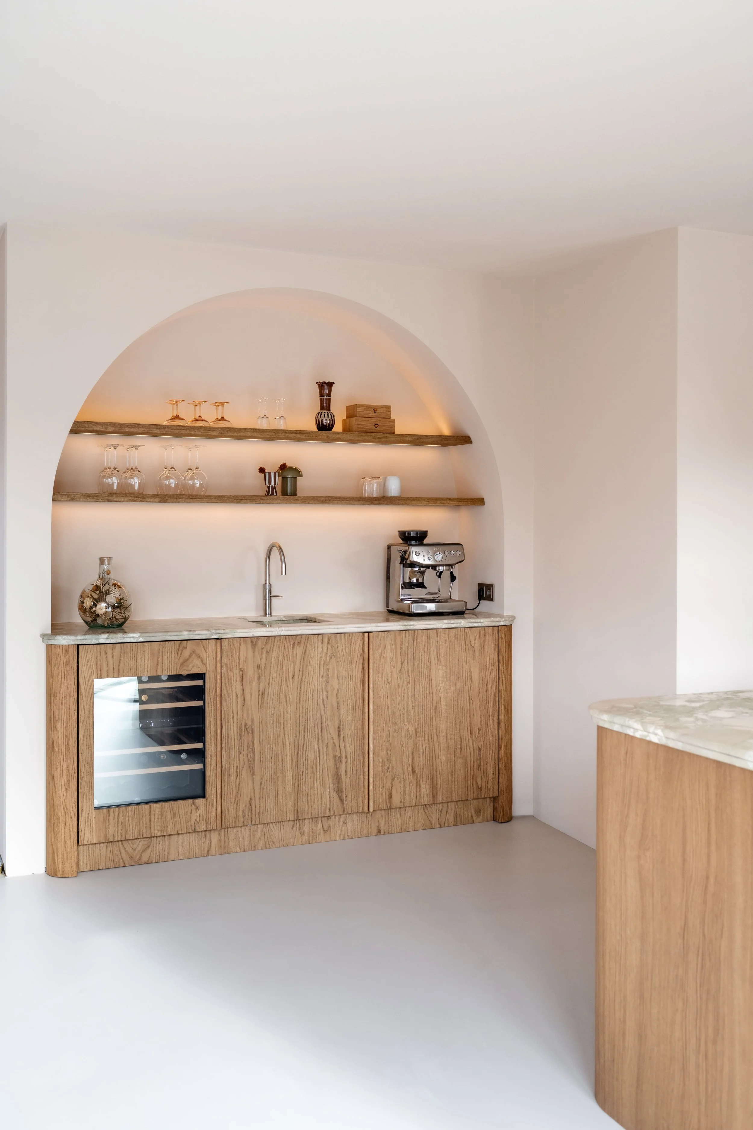 Maatwerk koffiehoek van eiken fineer met zwevende planken in een gestucte ronding en natuurstenen werkblad.