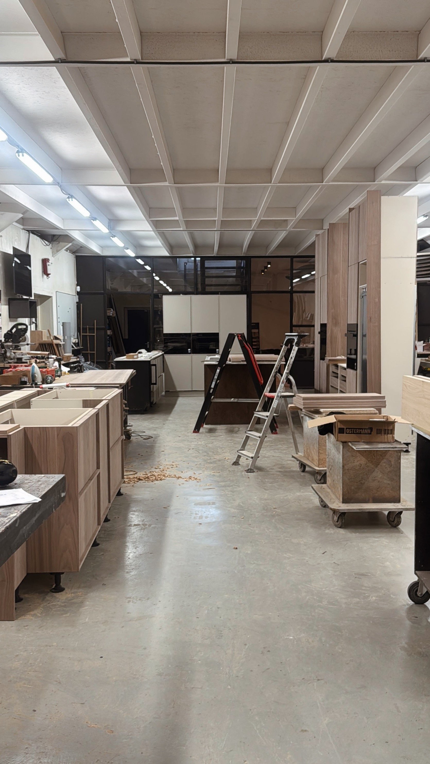Een interieur van een werkplaats met houten kasten en meubels in de bouw, ladder, arbeidsmaterialen en platen op wielen.