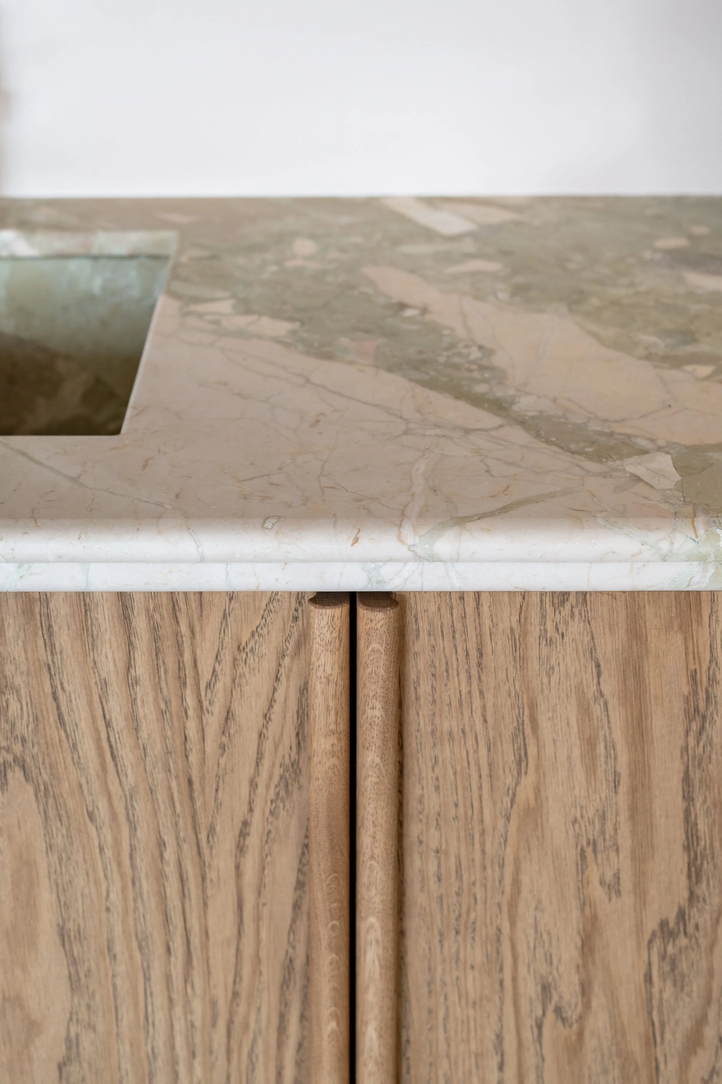 Detail van een maatwerk keuken met eiken fineer, geïntegreerde houten handgrepen en een natuurstenen werkblad.