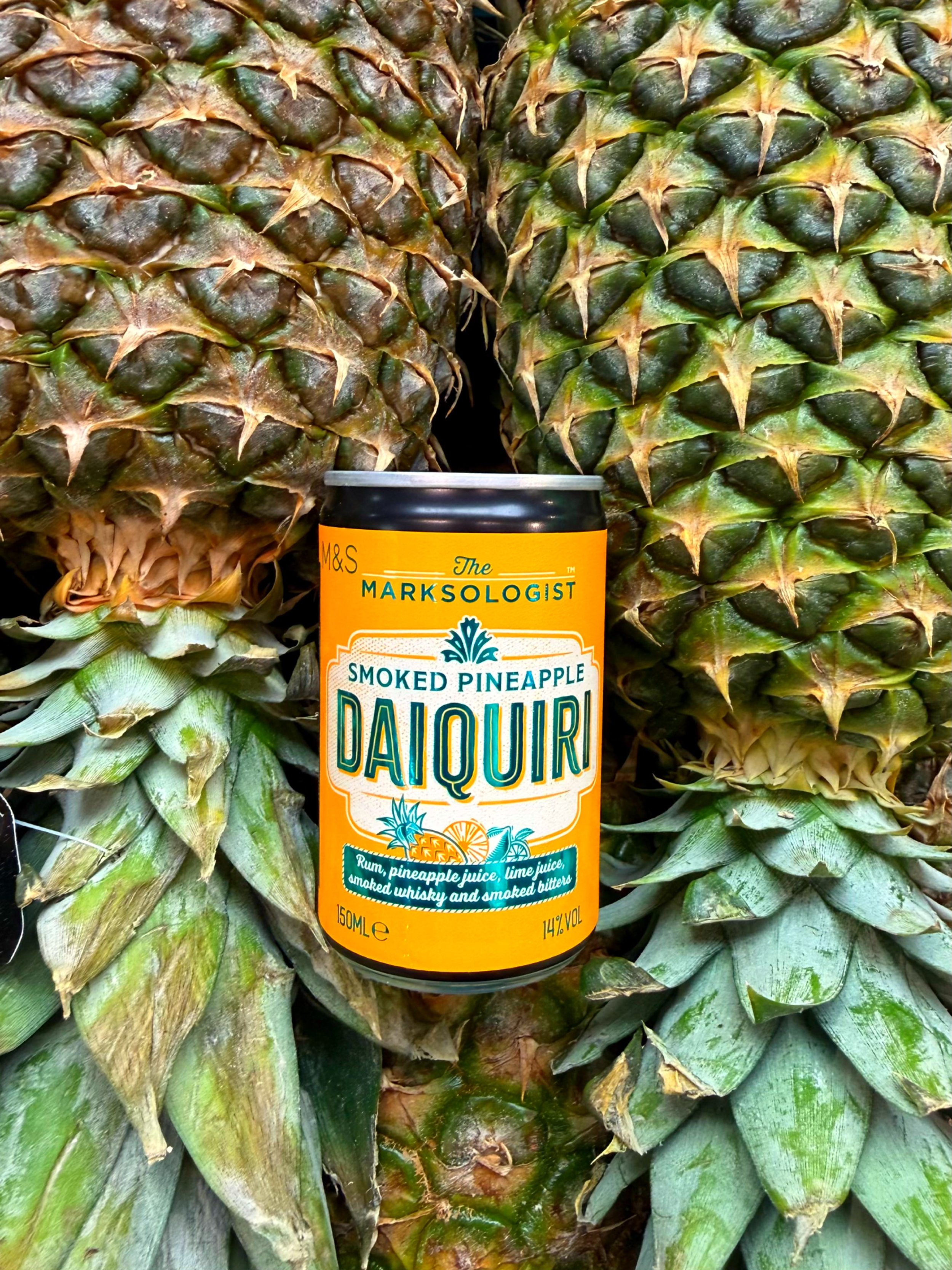 Close-up of two ripe pineapples with a can of daiquiri flavored drink placed between them.