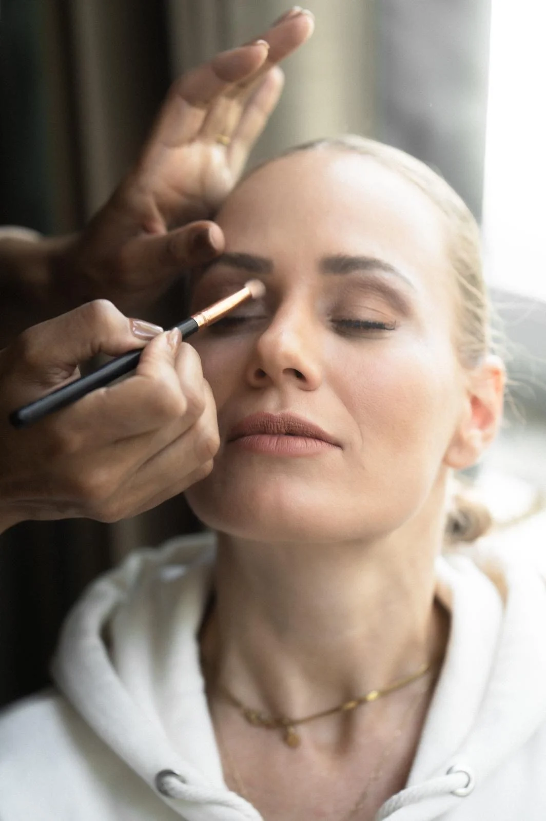 Eine Frau erhält professionelles Augen-Make-up, während sie entspannt mit geschlossenen Augen sitzt.