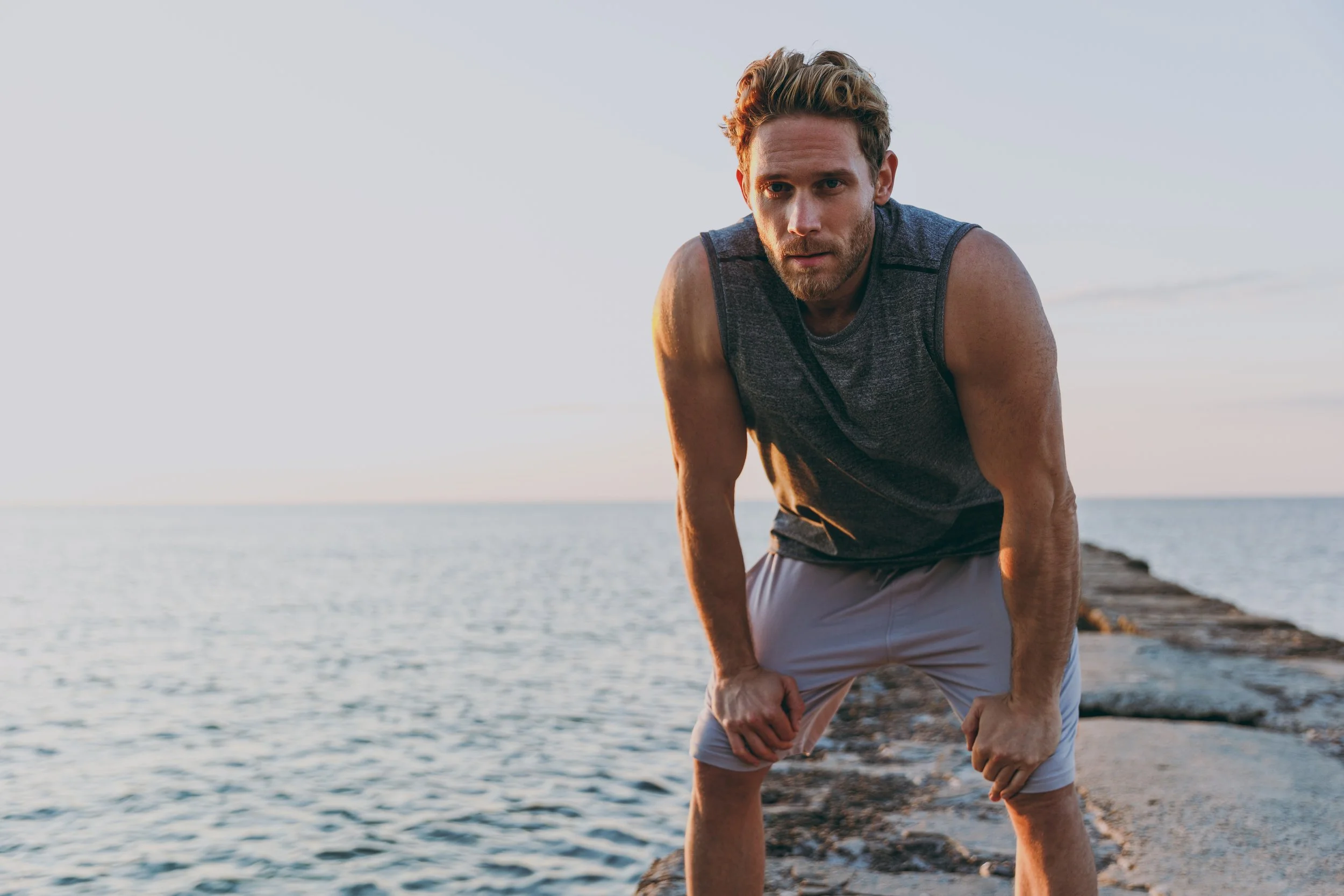 A man in workout clothes performing a push-up on a rocky beach during sunset