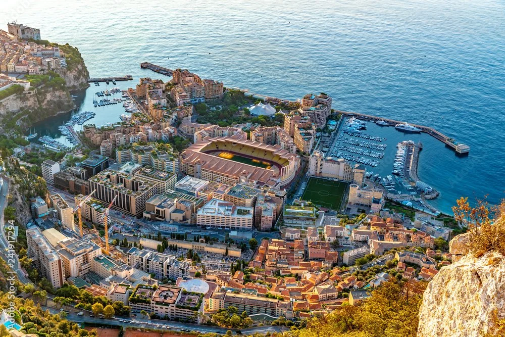 AS Monaco football stadium with aerial view of a coastal city with buildings, a stadium, marina, and ocean.