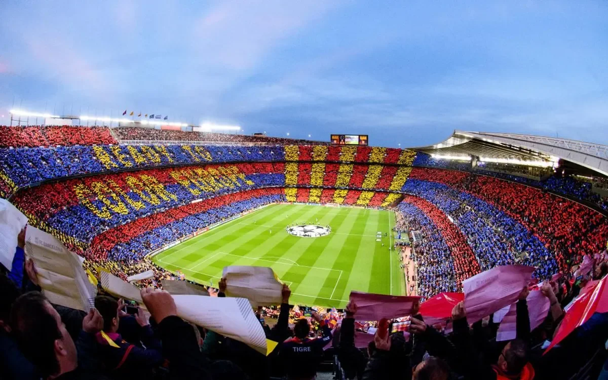 Barcelona football fans in the Nou Camp holding coloured papers to form a mosaic for a football game.