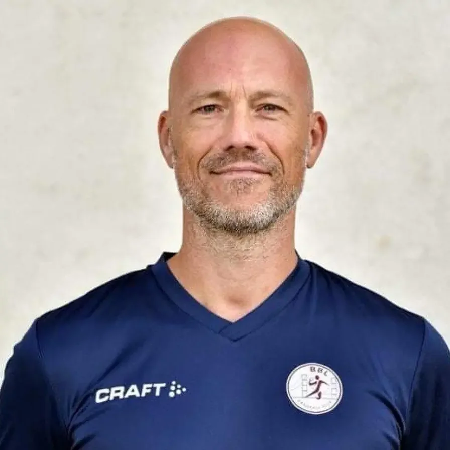Un homme à la tête chauve, portant un maillot de football bleu avec un logo de club de football.