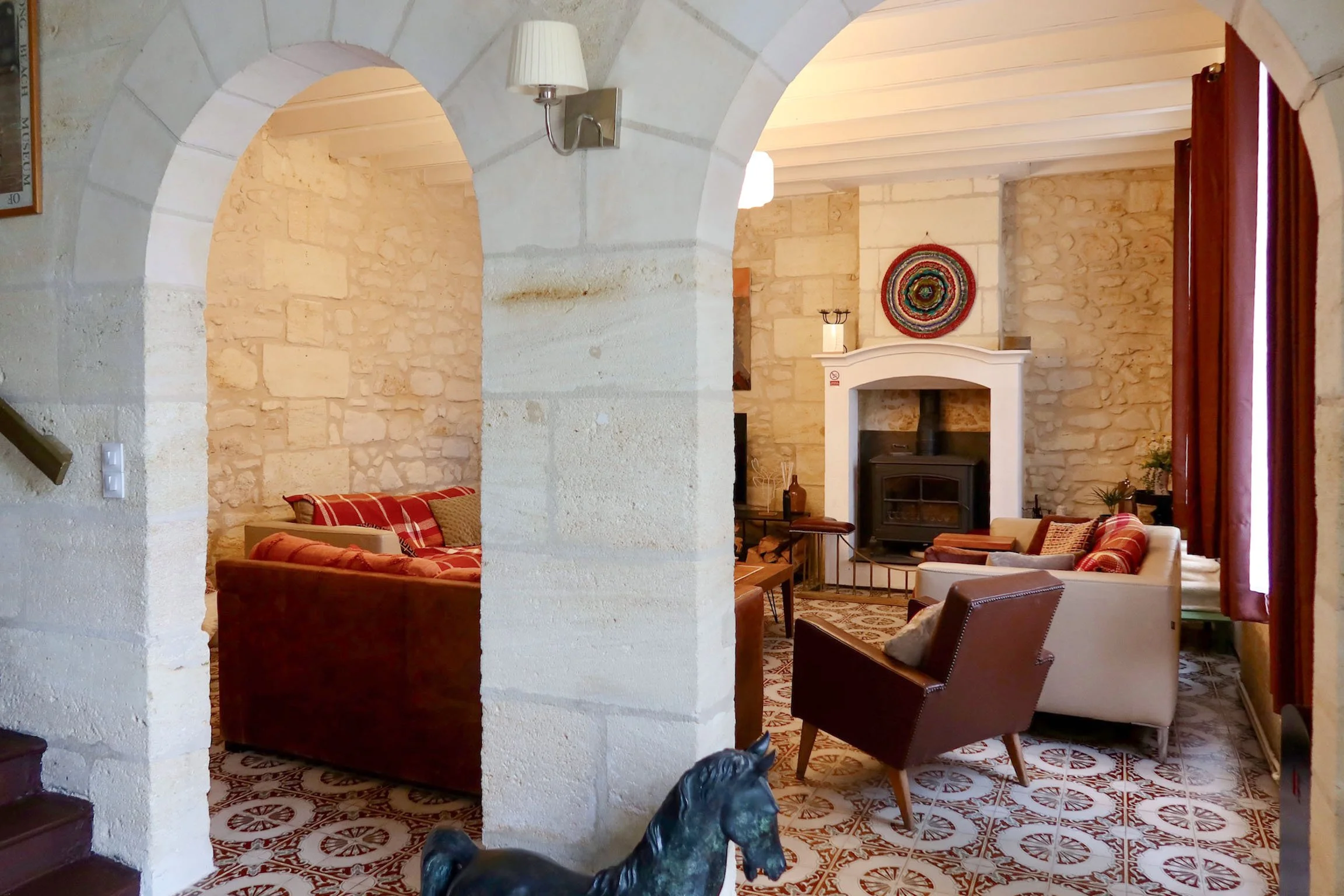 Intérieur d'une salle de séjour avec murs en pierre, cheminée, et fauteuils en tissu avec motif tartan rouge et beige.
