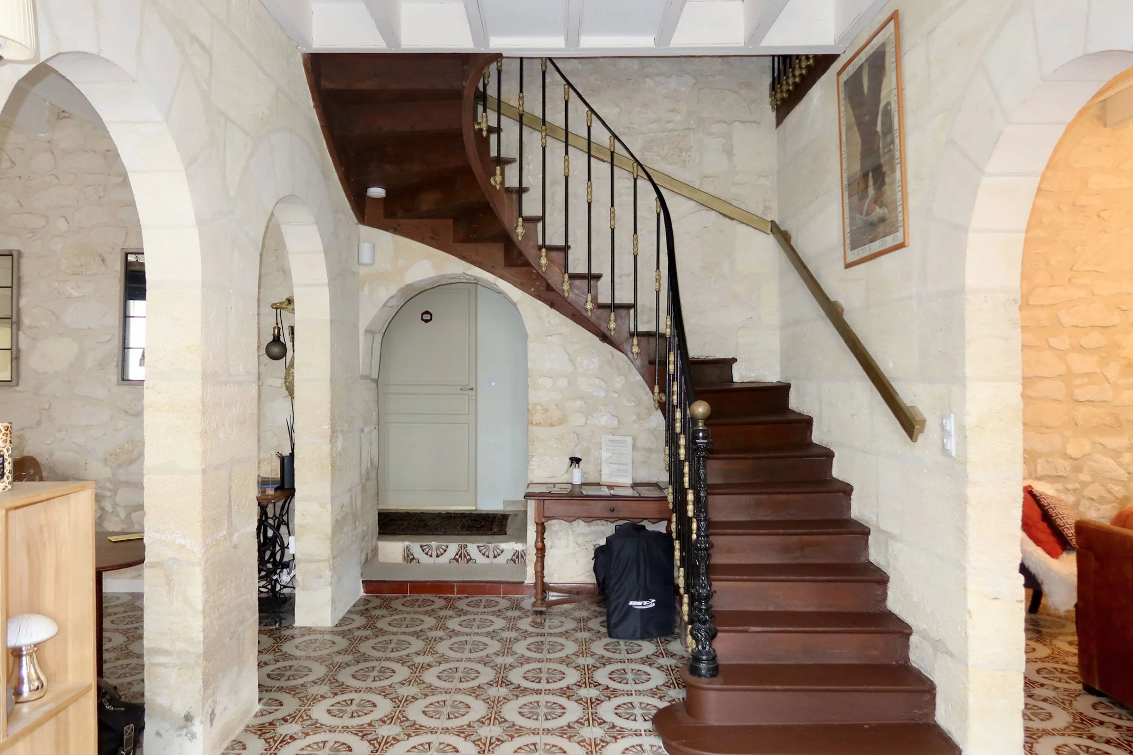 Escalier en bois courbé avec rambarde en métal à ornement doré, murs en pierre et décoration intérieure chaleureuse.