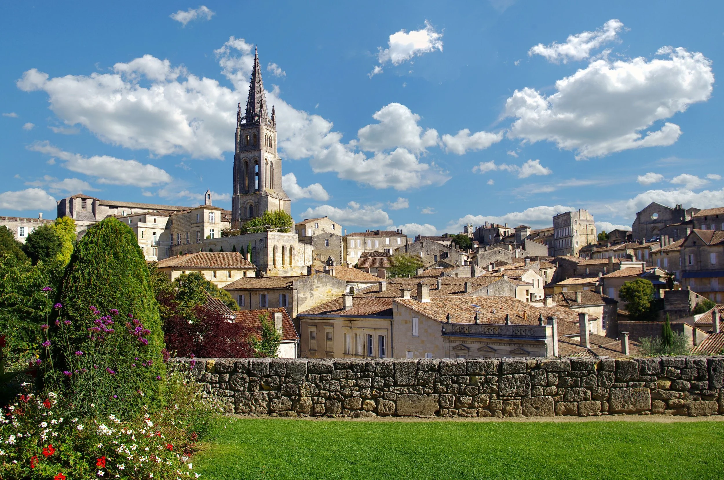 Une vue de la vieille ville de Toulouse, avec la cathédrale Saint-Étienne dominant le paysage, des maisons anciennes aux toits en tuiles et un ciel bleu parsemé de nuages blancs.