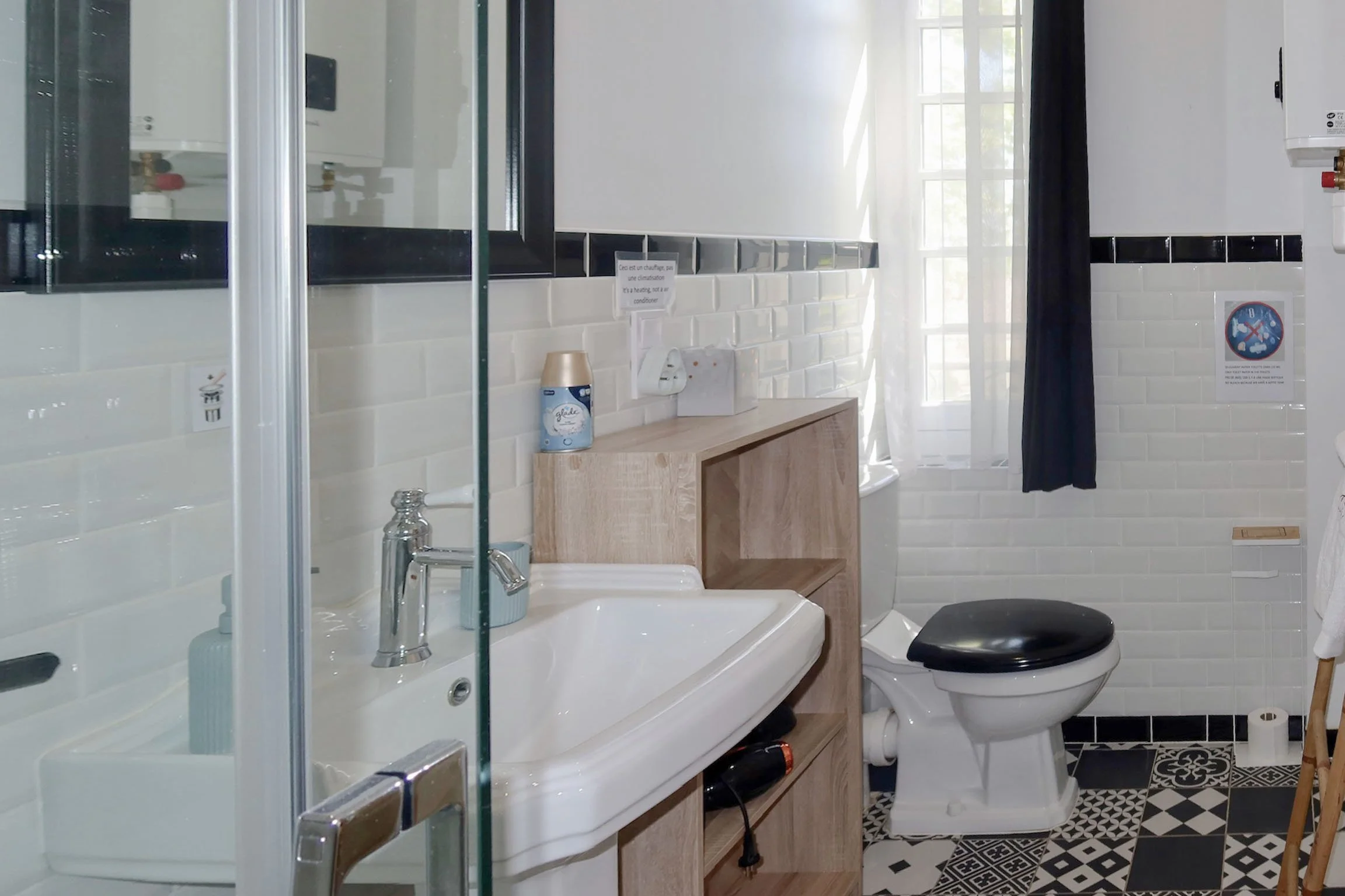 Salle de bain avec lavabo, miroir, toilette, sol à motifs noirs et blancs, fenêtre avec rideau noir, panneaux en tuiles blanches et noir