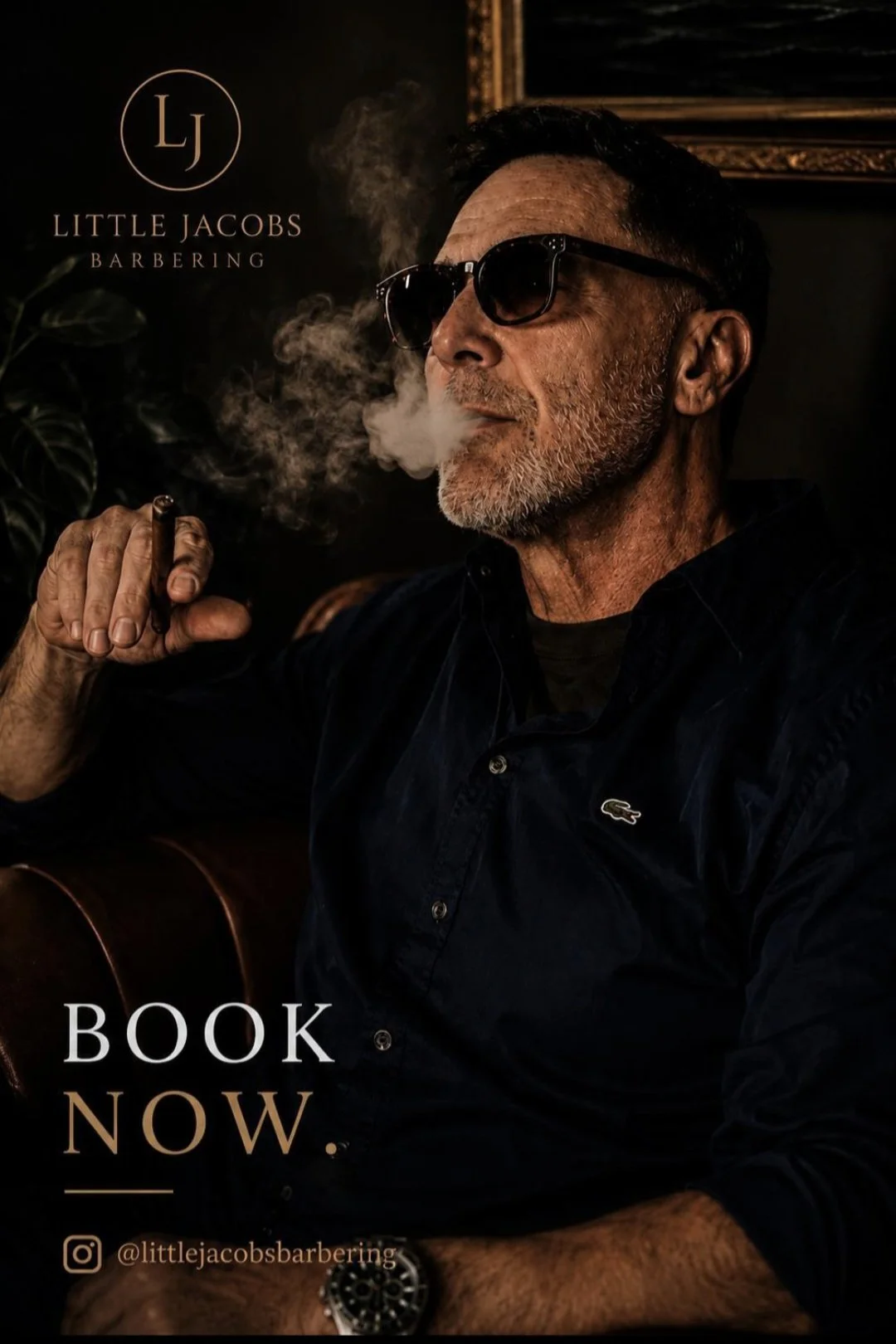 A man with gray beard and sunglasses smoking a cigar, wearing a dark jacket with a Lacoste logo, sitting indoors. A plant is visible in the background, along with a framed picture and a logo reading 'Little Jacobs Barbering'. The text on the image re