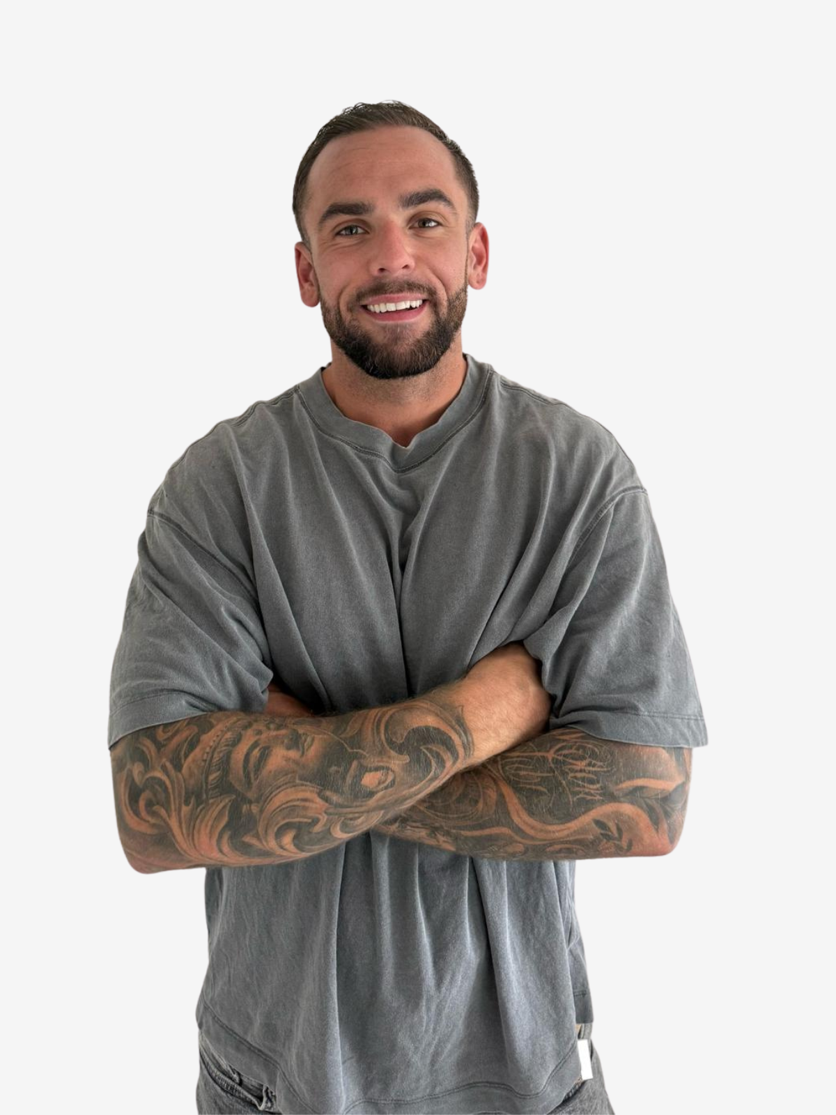A smiling man with short dark hair and a beard, wearing a gray T-shirt with tattooed arms, standing against a plain white background.