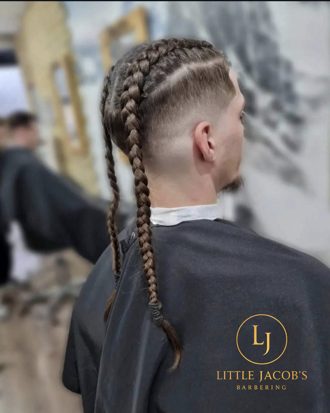 Man with a detailed braided haircut at a barber shop, wearing a barber cape, with the Little Jacob's Barbering logo in the bottom right corner.