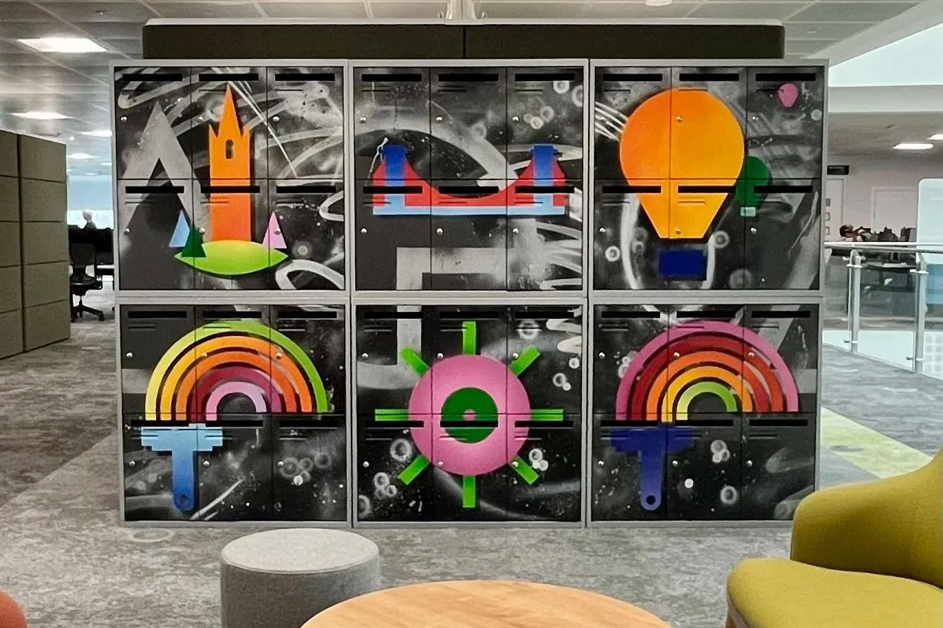 Colorful, cartoonish artwork on a locker unit in an office, featuring a castle, bridge, light bulb, rainbow, gear, and musical note, with a space-themed black background.