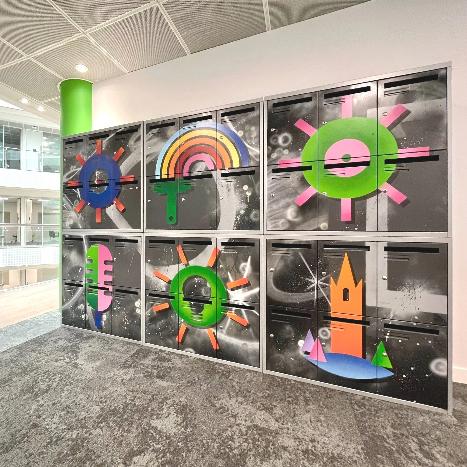 A wall of lockers with colorful, abstract digital artwork resembling safety or warning symbols, including a rainbow, a light bulb, gears, and a starburst in a modern indoor setting.