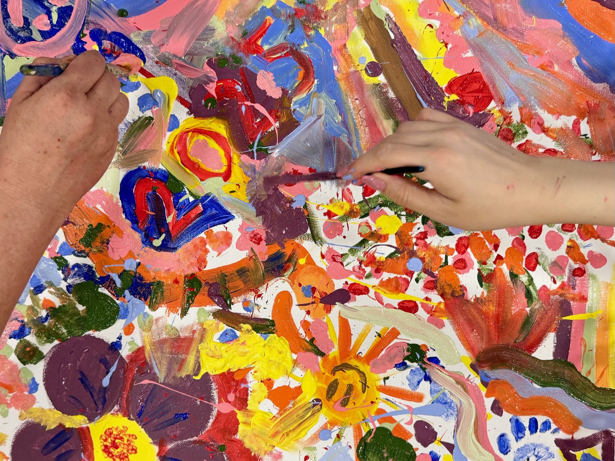 Hands painting an abstract colorful canvas with various brush strokes and splashes of paint.